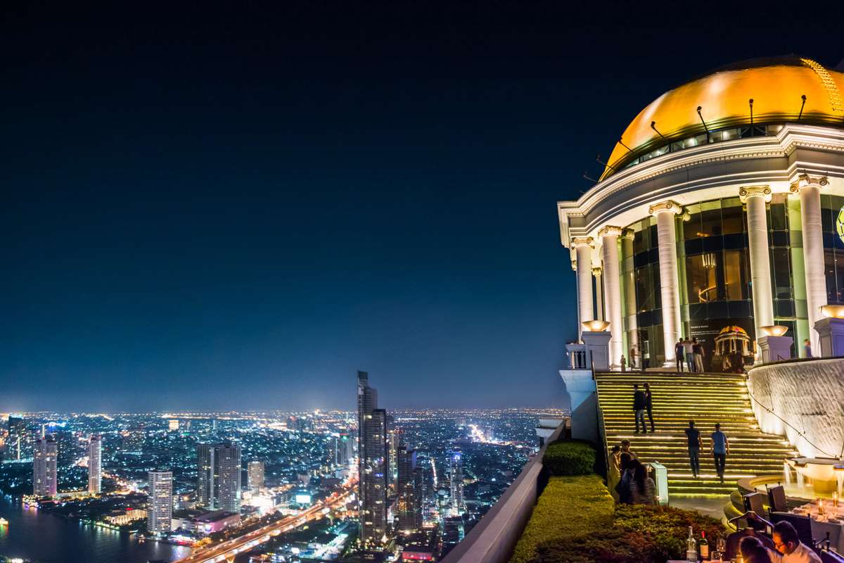 A night view of a lit city skyline and harbor from a balcony next to a domed building with golden accents.