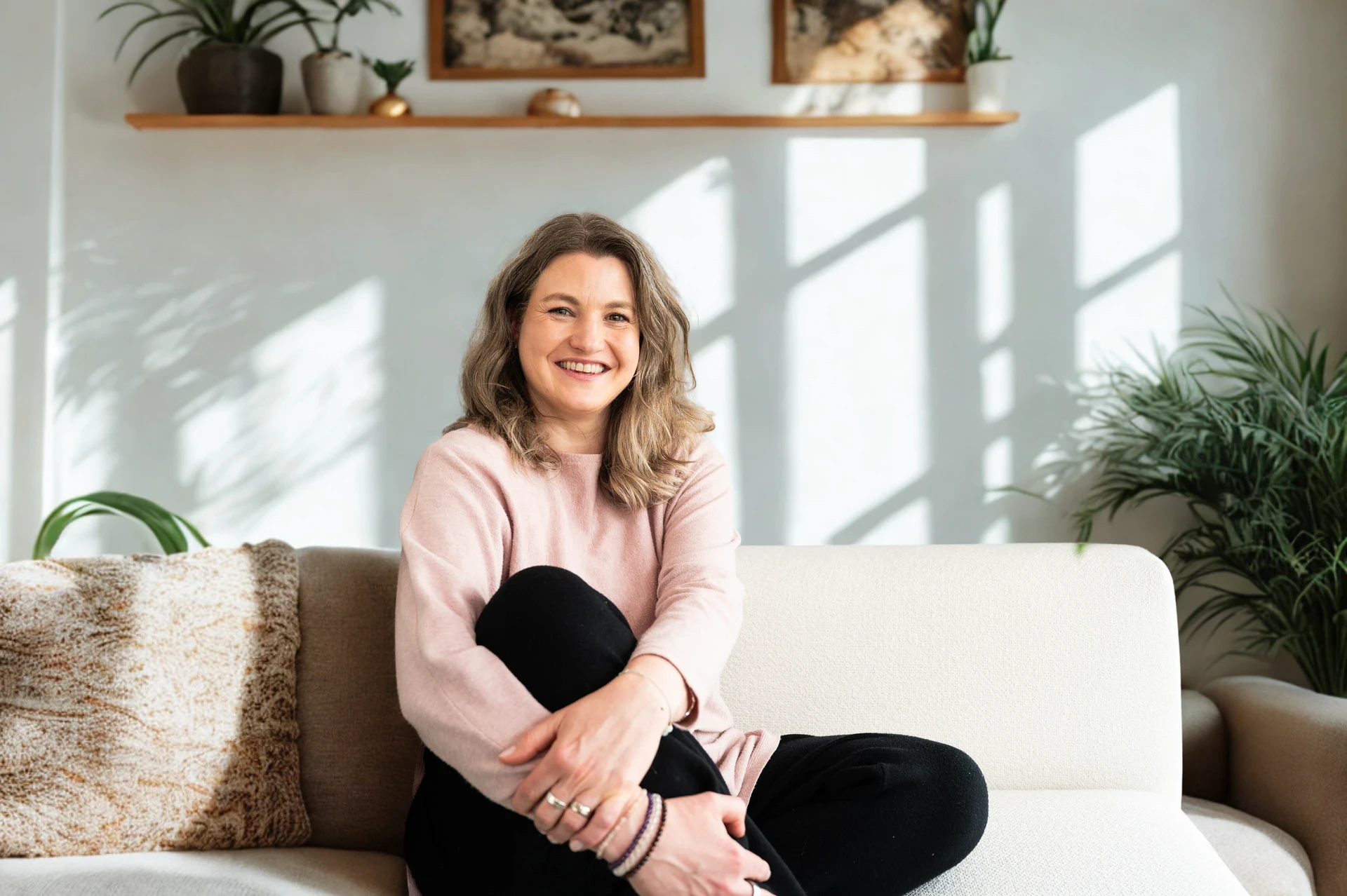 Four friends laughing together outdoors in natural light, dressed in neutral casual outfits.