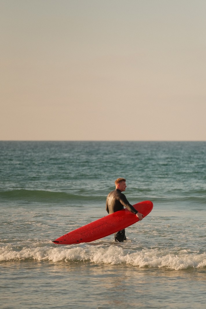 Surfer with a surfboard in the ocean at sunset