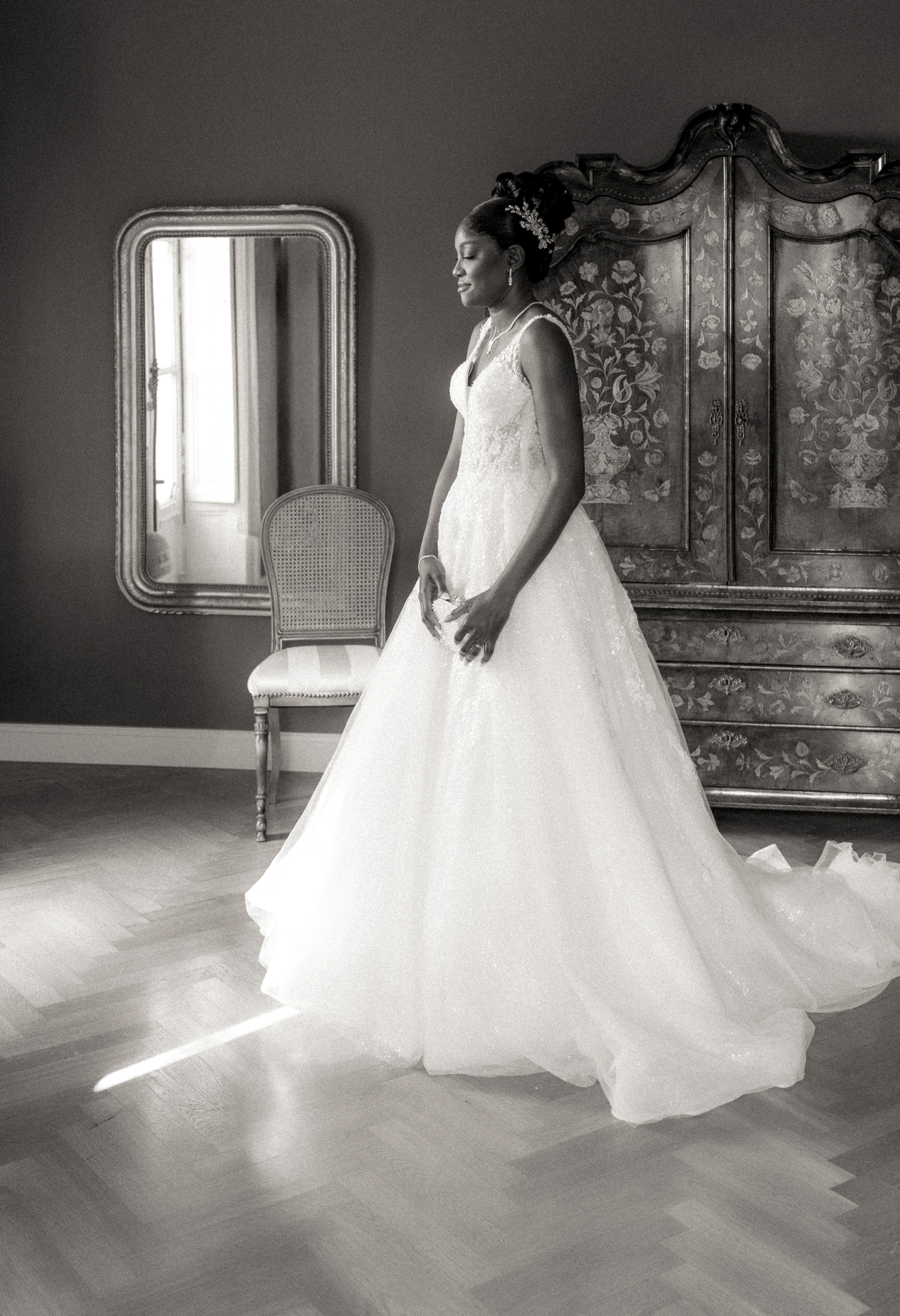 Mariée en robe devant une armoire ancienne et un miroir, photographie de mariage en noir et blanc