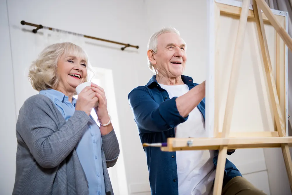 happy senior couple painting picture on easel