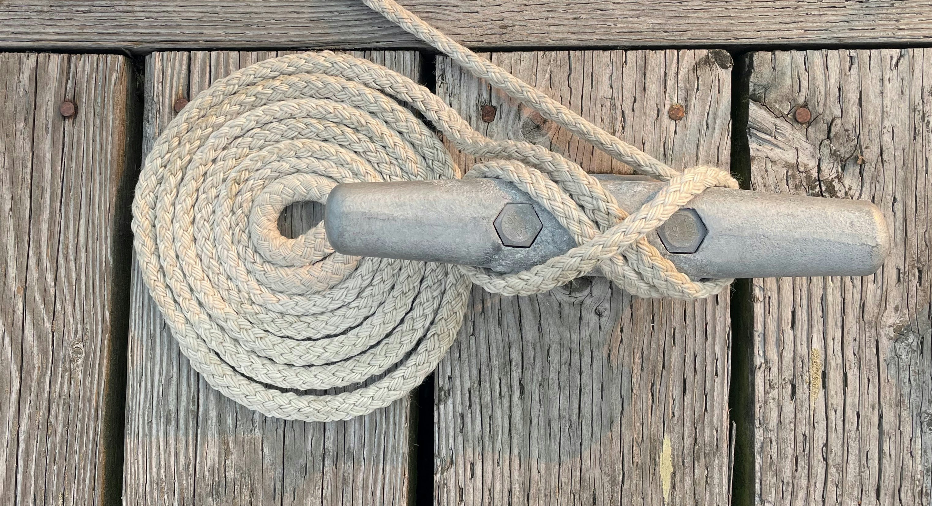 A dock line coiled and tied off on a metal cleat on wooden planks