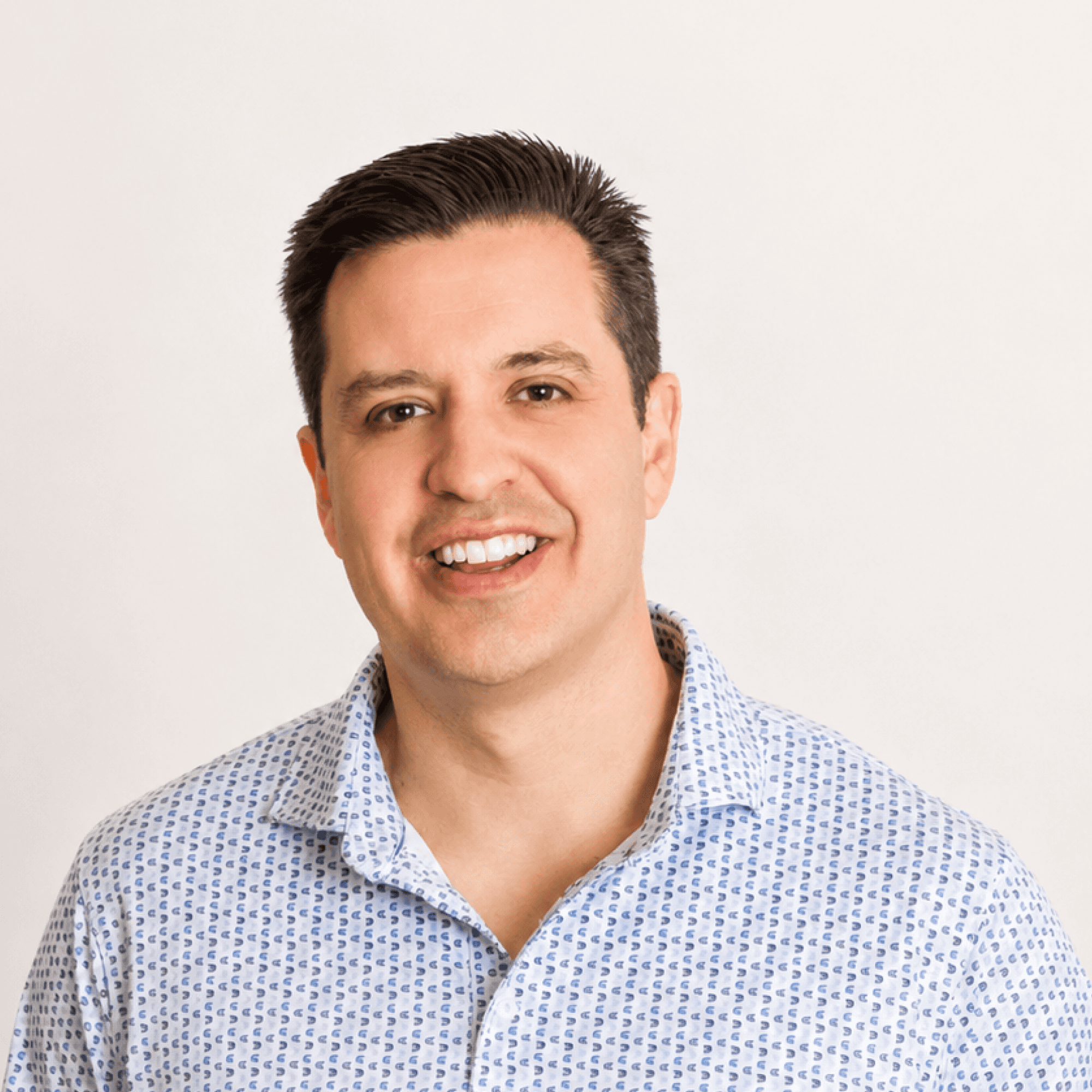 Professional headshot of a MelodyArc team member, a smiling man with short dark hair in a light blue patterned shirt.
