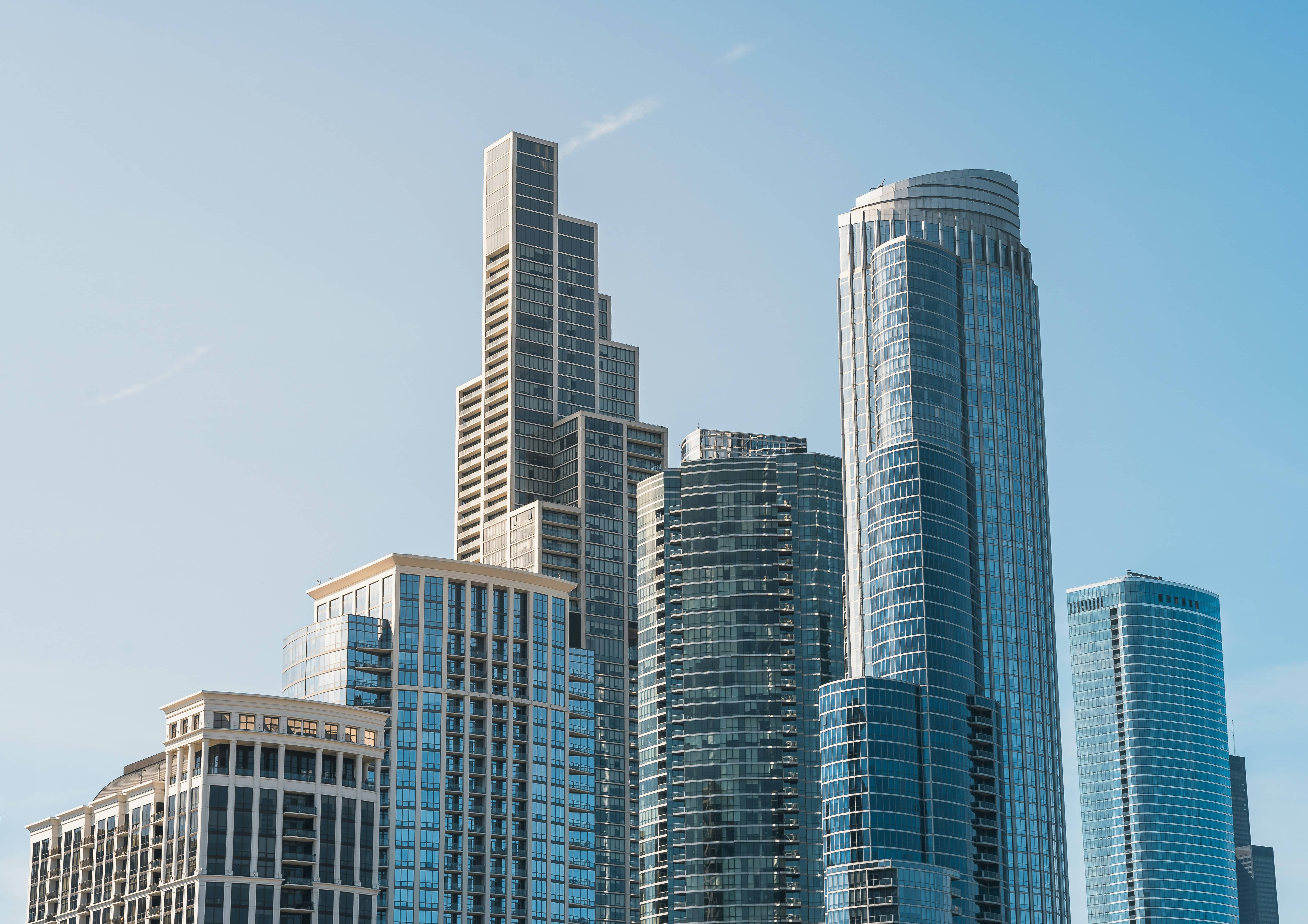 Cluster of modern glass and stone high-rises against a clear sky, with a stepped tower and a curved glass skyscraper.