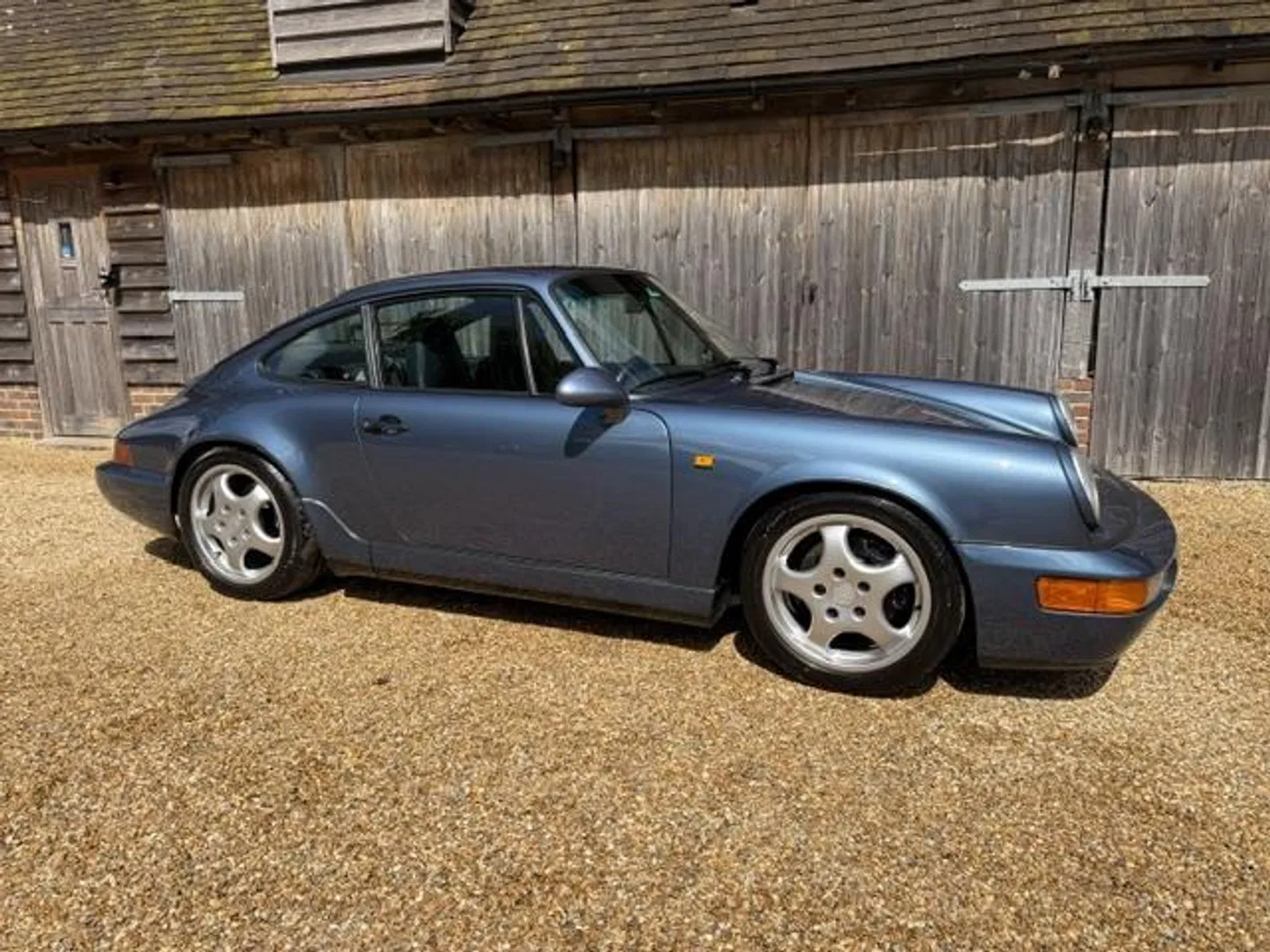 Full side profile of the Porsche 964 C4 in front of a wooden barn