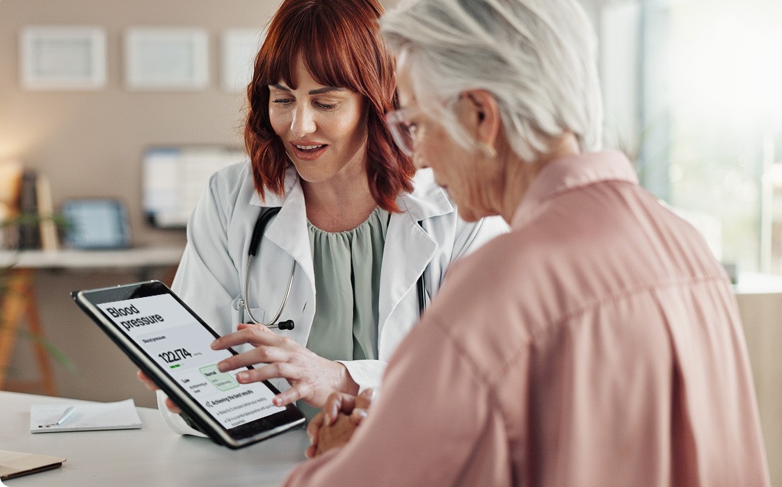 A female doctor and an older woman looking at an iPad tablet, that's showing Blood Pressure results.