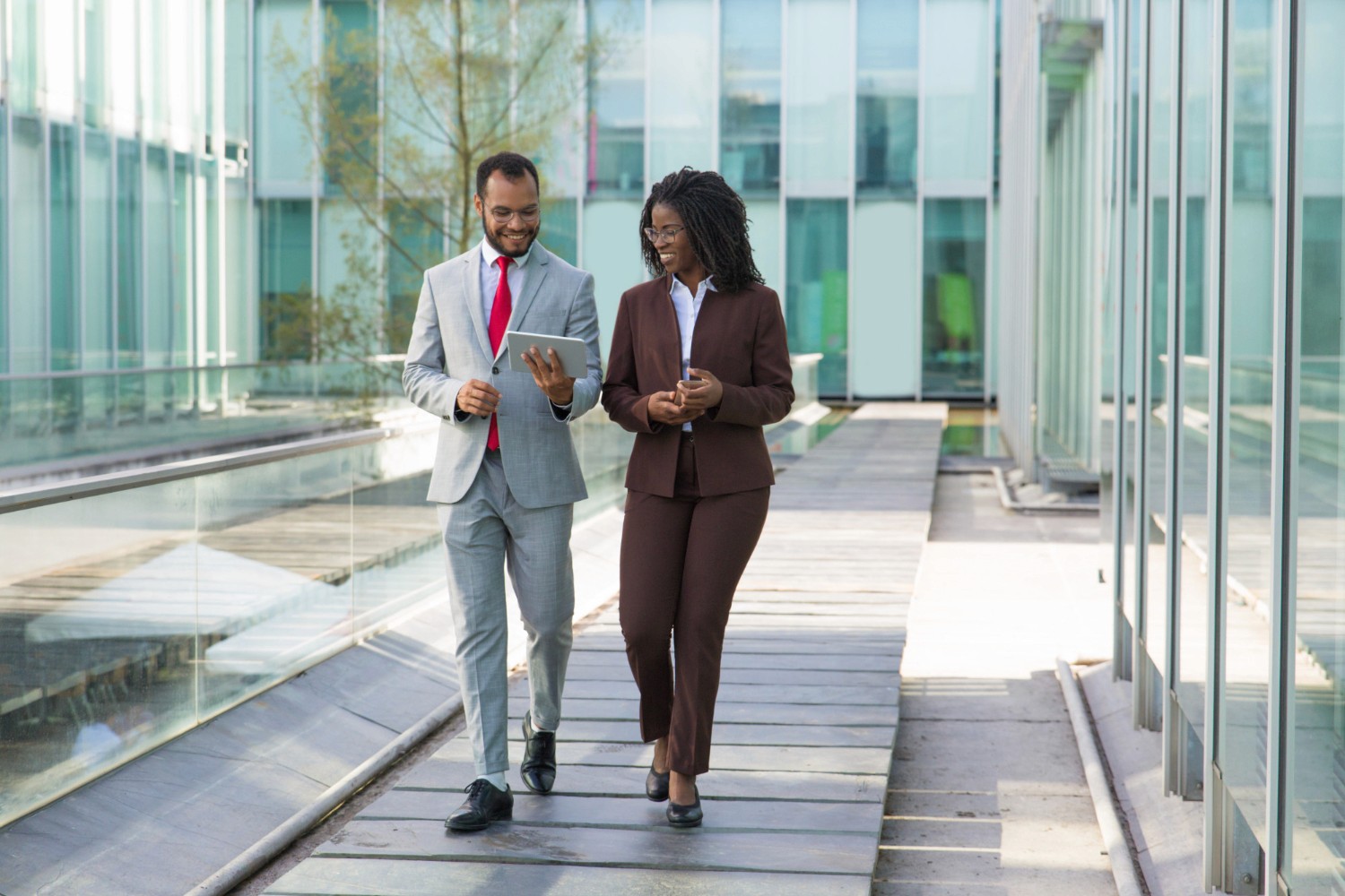 Two business professionals walk along a modern glass walkway, discussing how to obtain a jafza trade license.