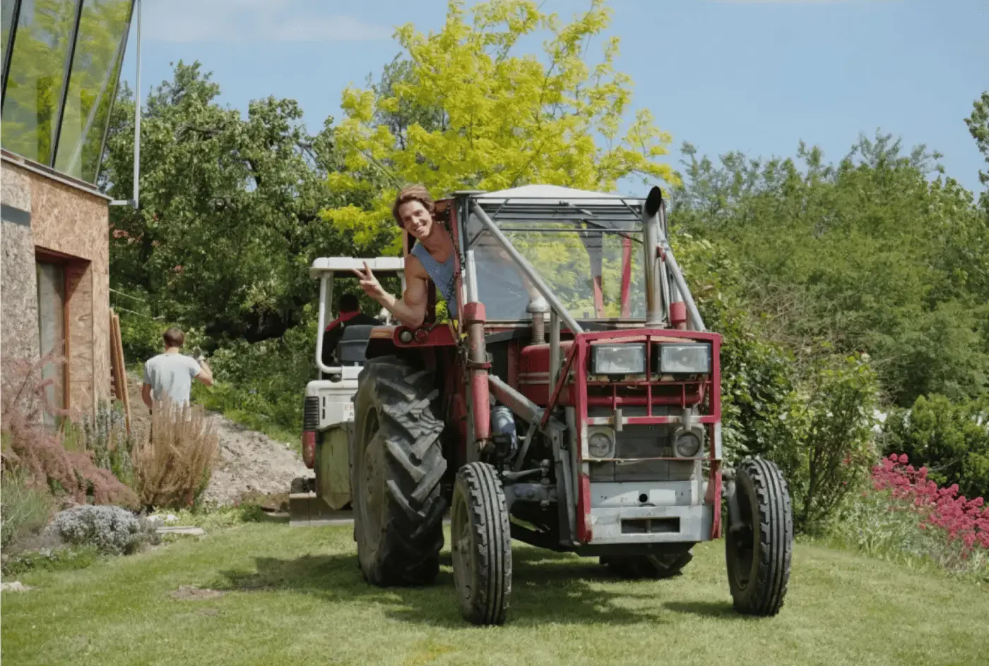 Markus Schmoltner winkt vom alten roten Traktor im Garten neben dem Chalet.