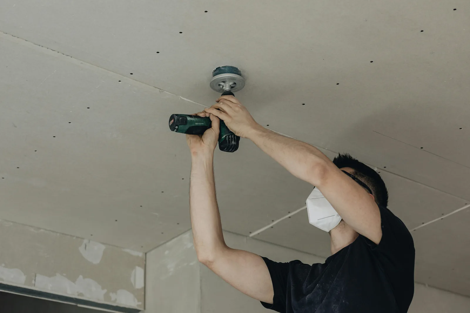 Worker drilling light fixture mount into drywall ceiling panel