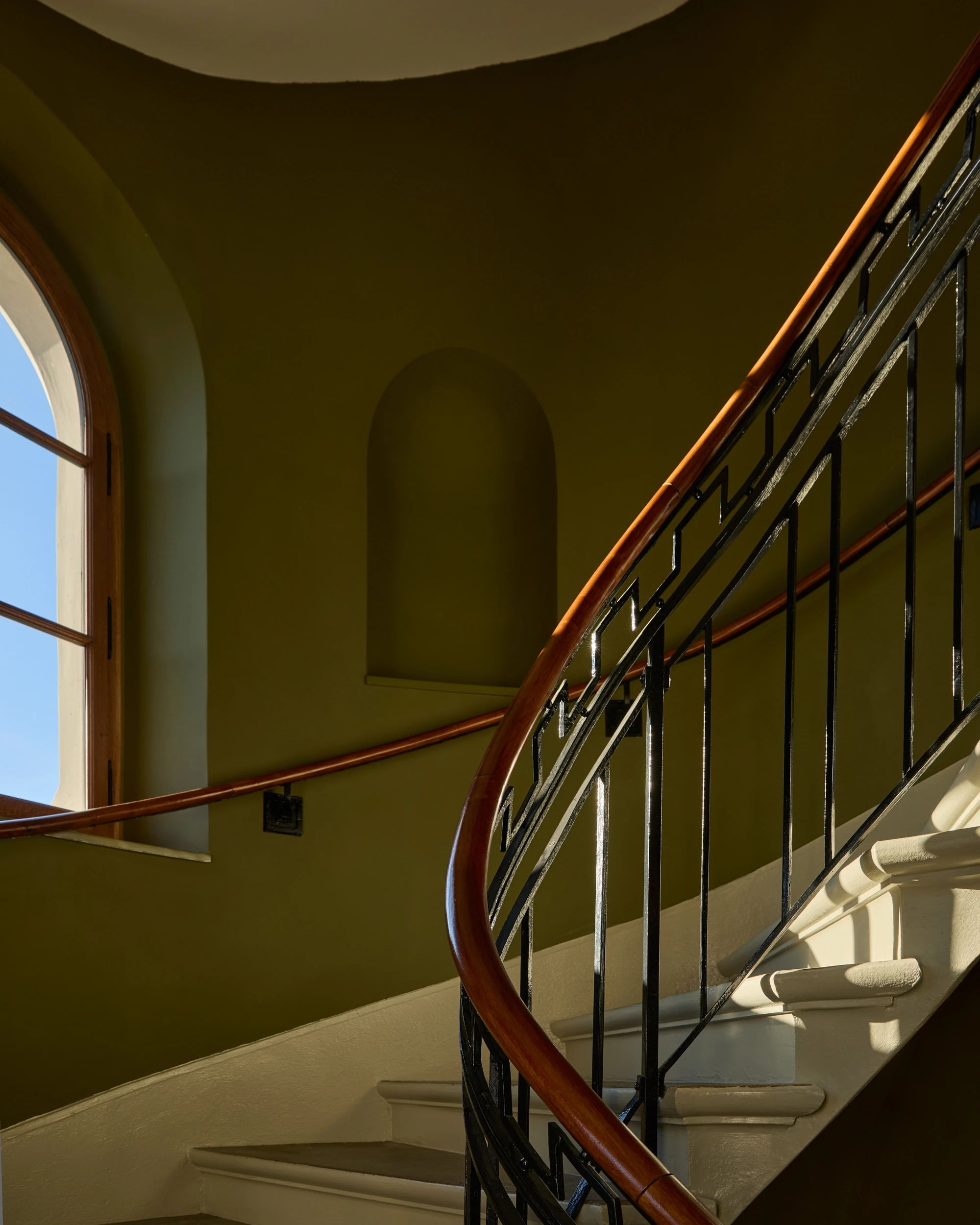 Escalier du XIXᵉ siècle du Château de Saint-Prex, avec rambarde en serrurerie, main courante en chêne et murs dans une teinte vert Empire.
