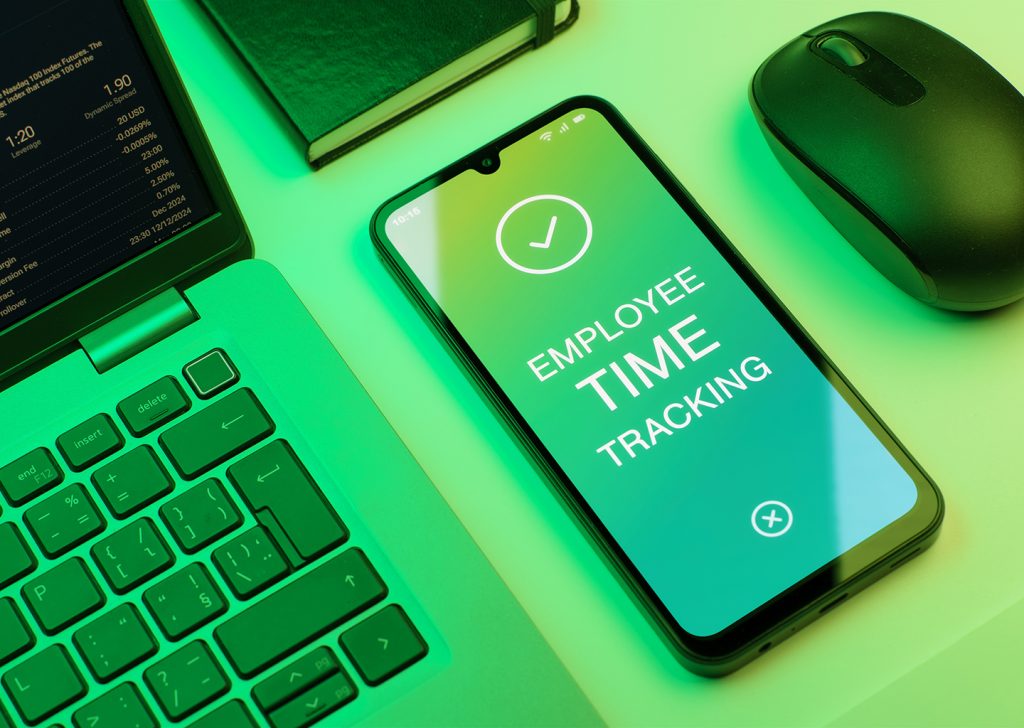 Su una scrivania, affianco al laptop aperto, uno smartphone mostra una schermata generica di una time tracking app