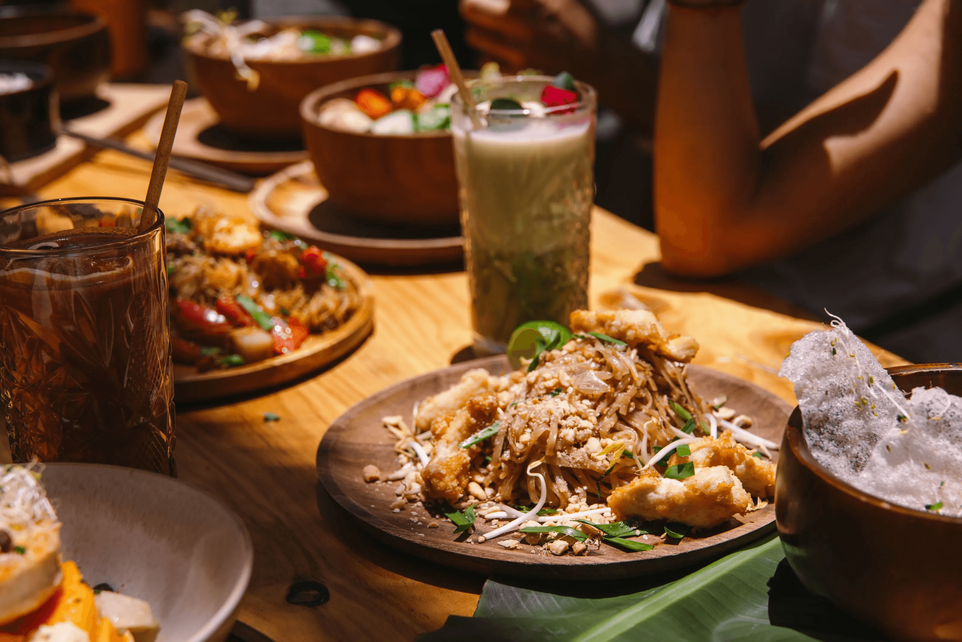 Pad Thai with peanuts and lime on a wooden plate, with cocktails and bowls in the background at Secret Garden, Lajares, Fuerteventura.