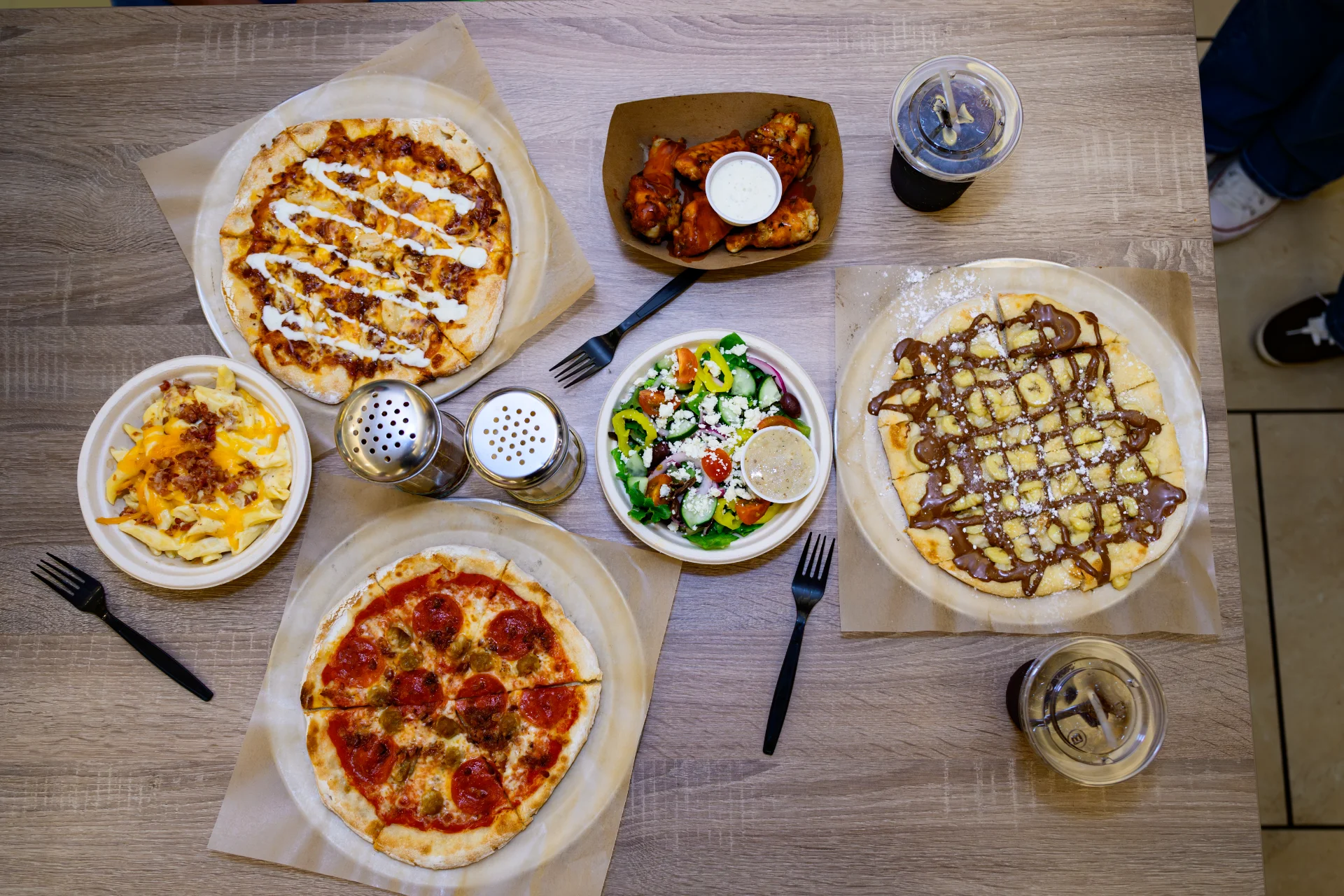 Overhead spread of pizzas, wings, salad, mac and cheese, and a dessert pizza at Urban Bricks Kitchen