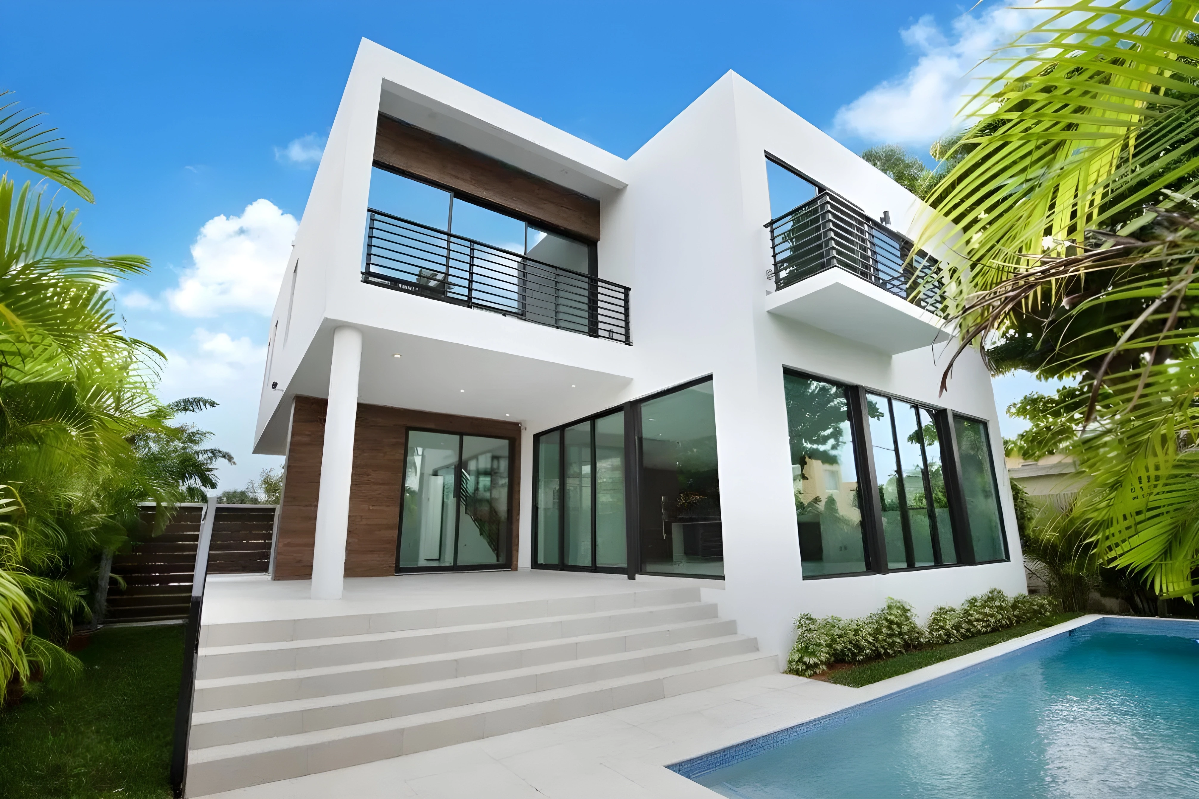 Modern two-story Miami home with white stucco, glass walls, balconies, and pool surrounded by tropical palms.
