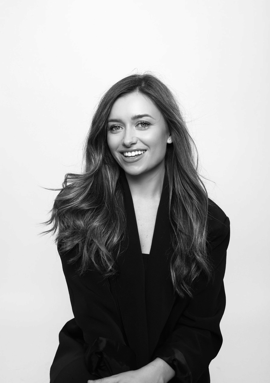 A smiling man with short hair stands with arms crossed, wearing a dark shirt against a neutral background.