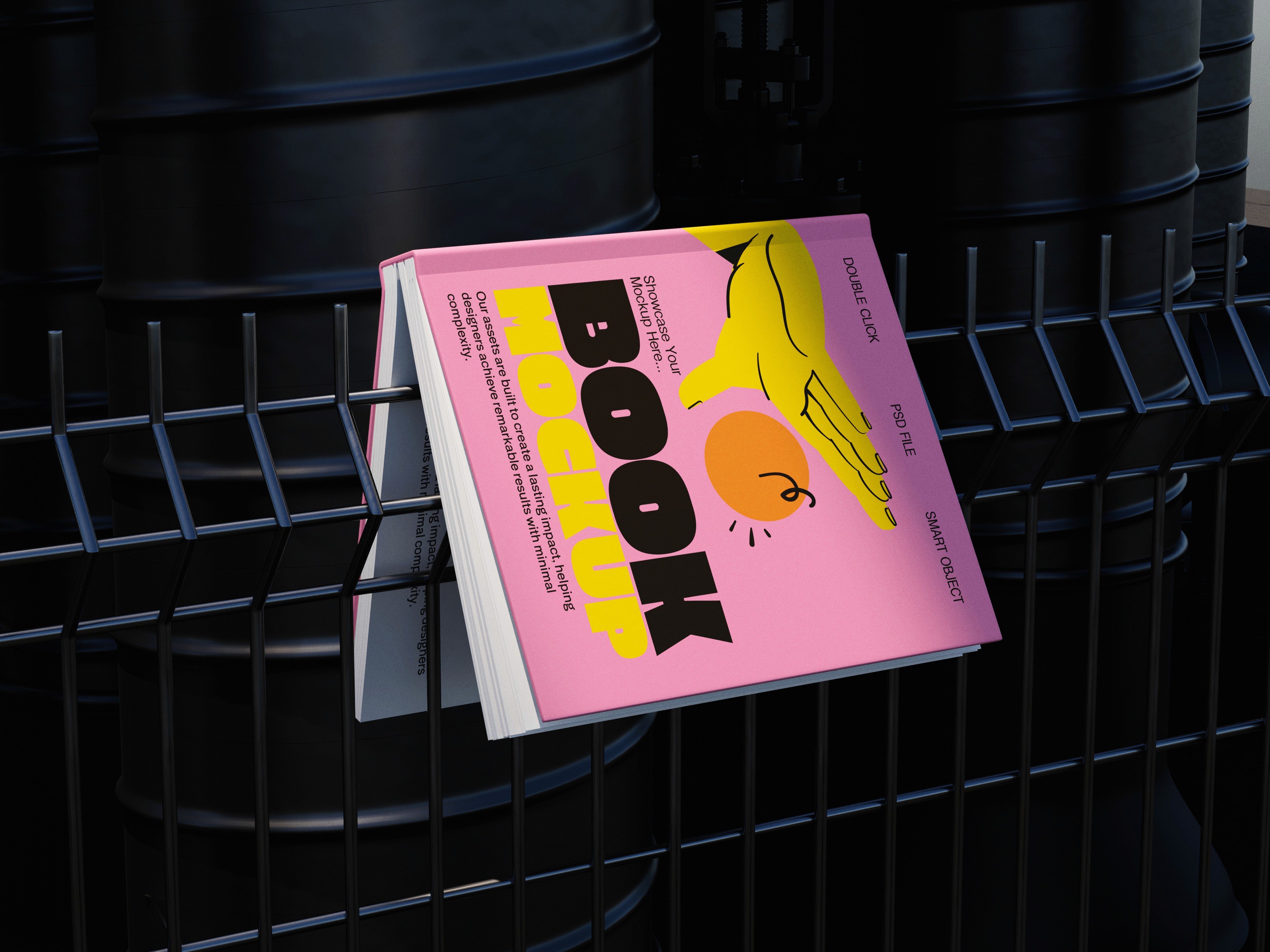 Pink book mockup with bold graphics caught in a dark metal fence in front of black barrels.