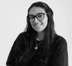 Smiling blonde woman with freckles in a white shirt, arms crossed, minimalist studio portrait.