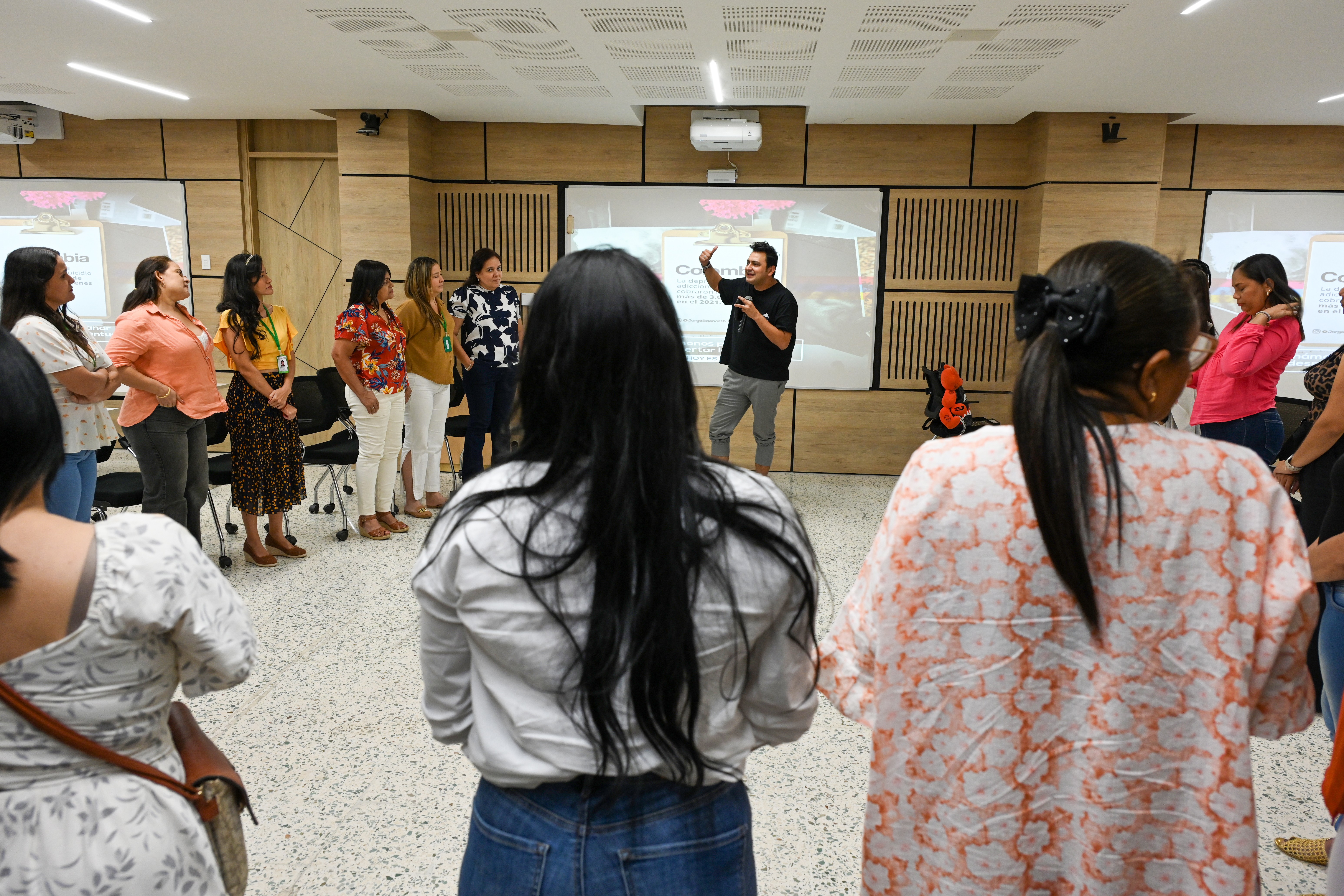 Jorge Baena guiando una dinámica grupal con un grupo de mujeres en un salón, todas de pie en círculo participando activamente en un taller vivencial sobre comunicación y liderazgo.