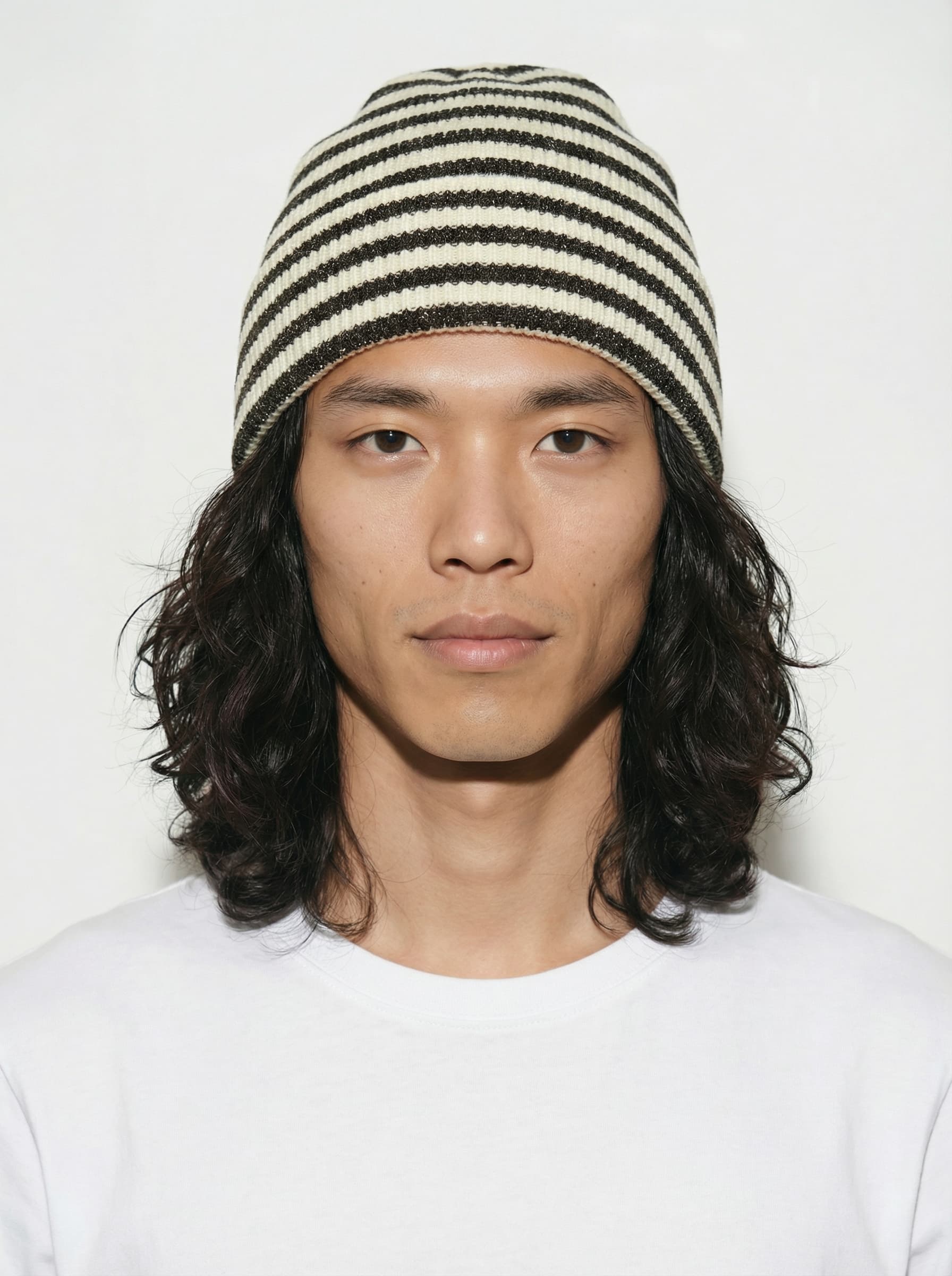 A person stands against a plain white background wearing a black baseball cap, a white oversized T-shirt, black pants, and white sneakers, exuding a casual fashion style.