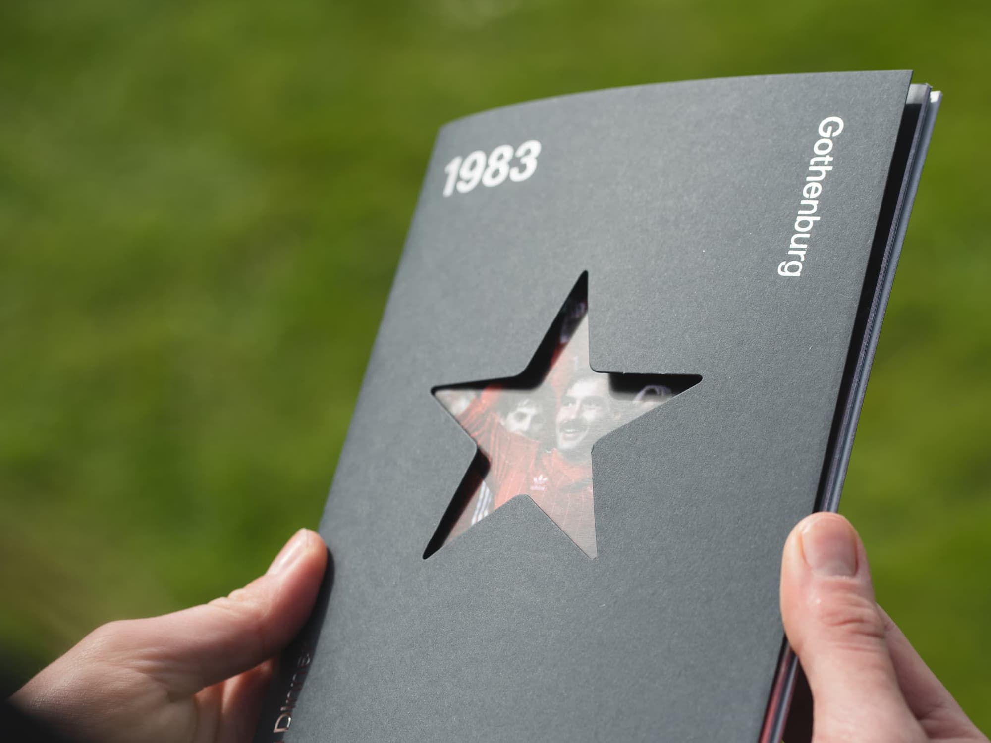 Football programme being held in hand outside in grassy area