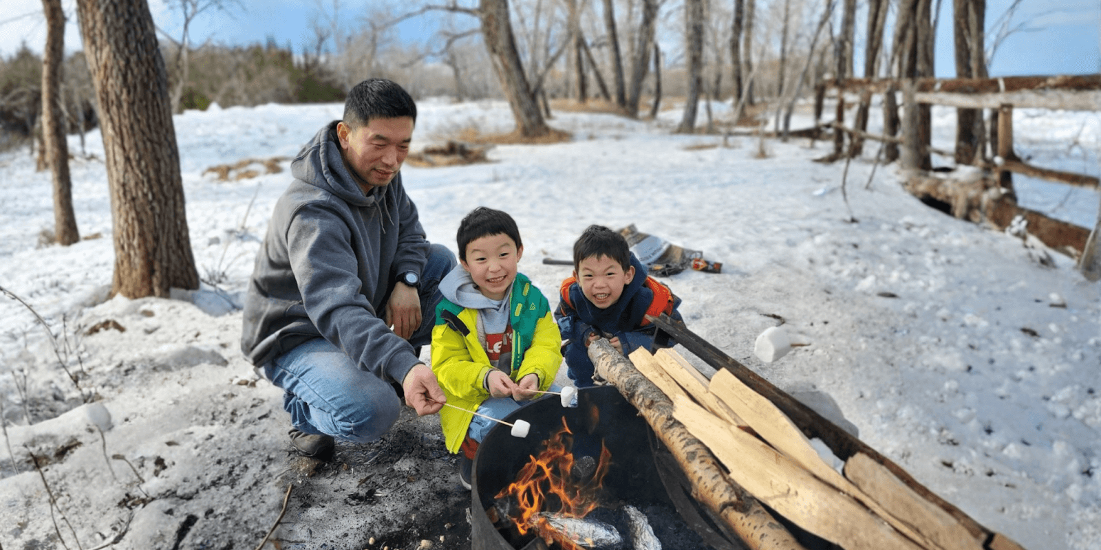 A father and his two children roasting marshmallows over a fire in the snow, enjoying a family outing.