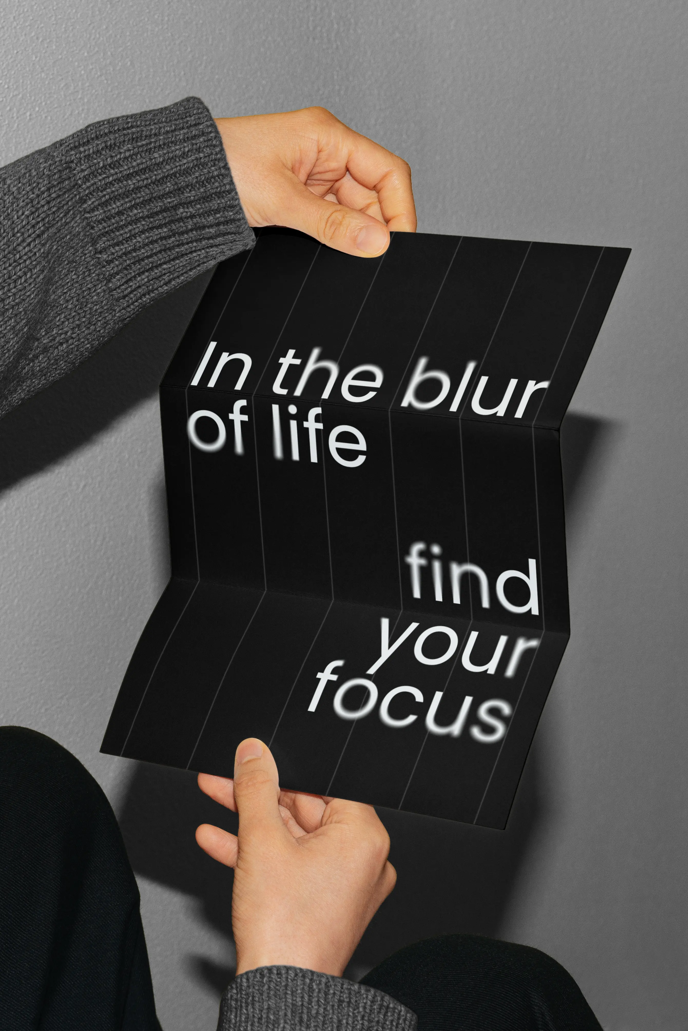 Black folded poster with the text 'In the blur of life find your focus' held by hands.