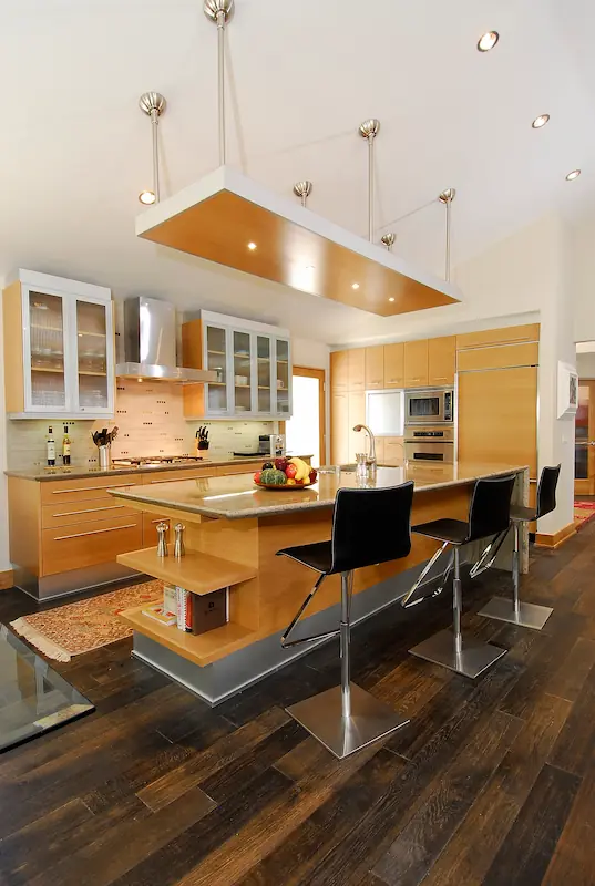 Modern kitchen with wooden cabinets, central island, hanging lights, and dark flooring. Irvine Transitional Modern. Photo by Chris Darnall.