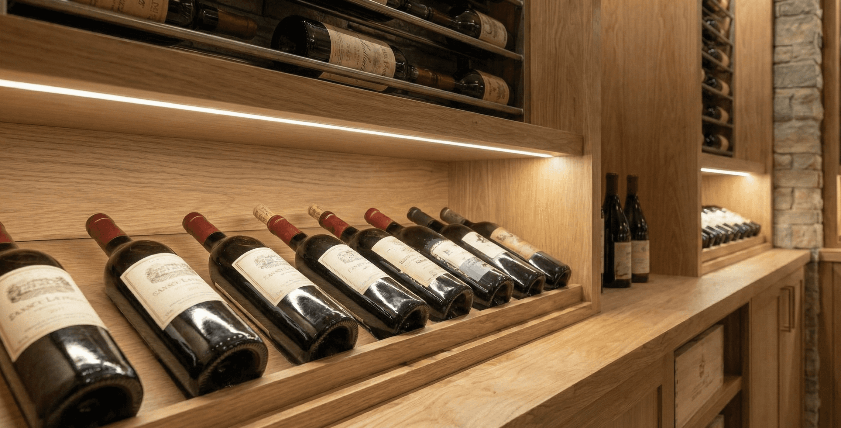 Label-forward bottle display on an oak shelf with recessed LED lighting and stone accents in a custom wine cellar