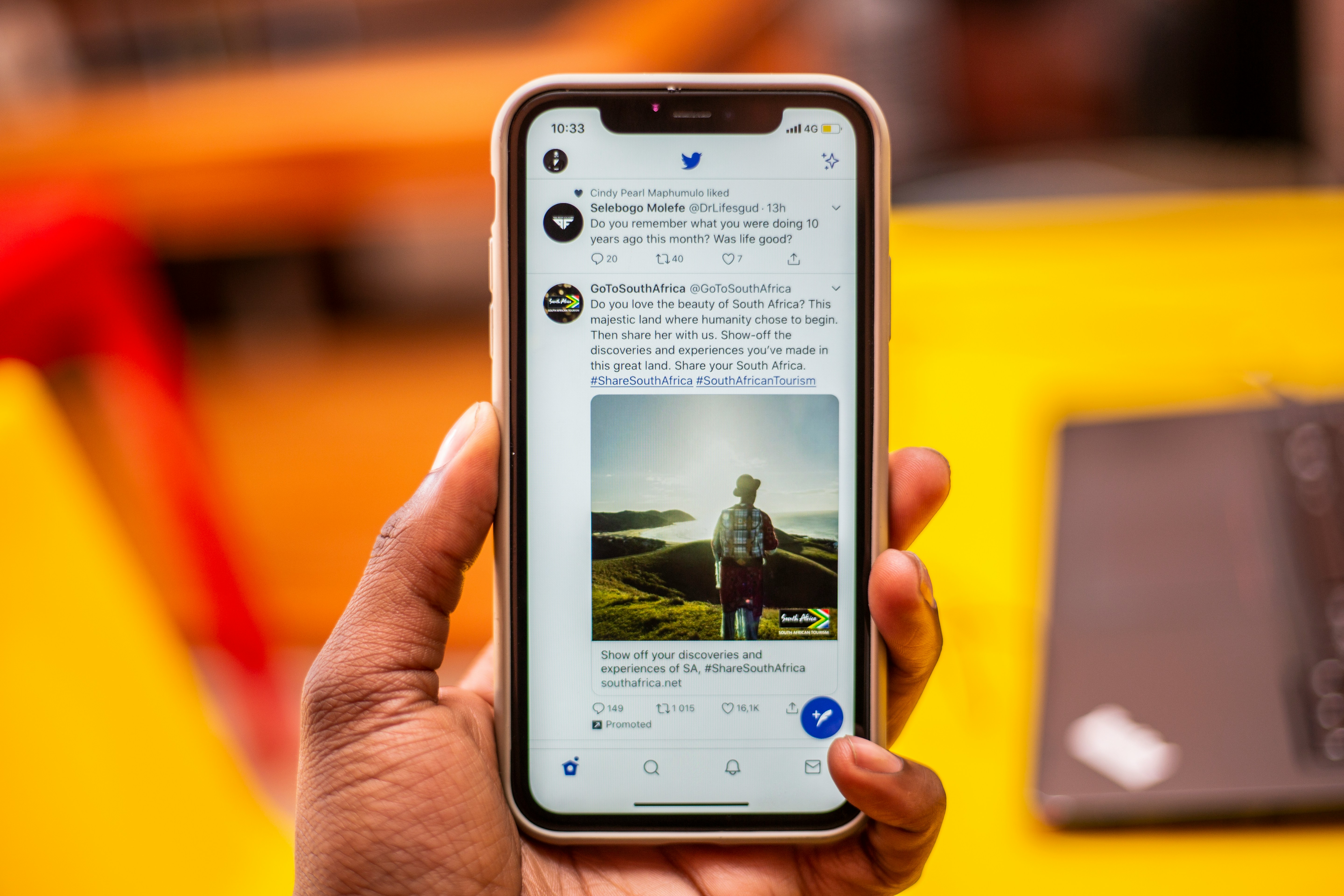 Person holding a smartphone displaying promoted posts on the X app, showing examples of in-feed ads and engagement.