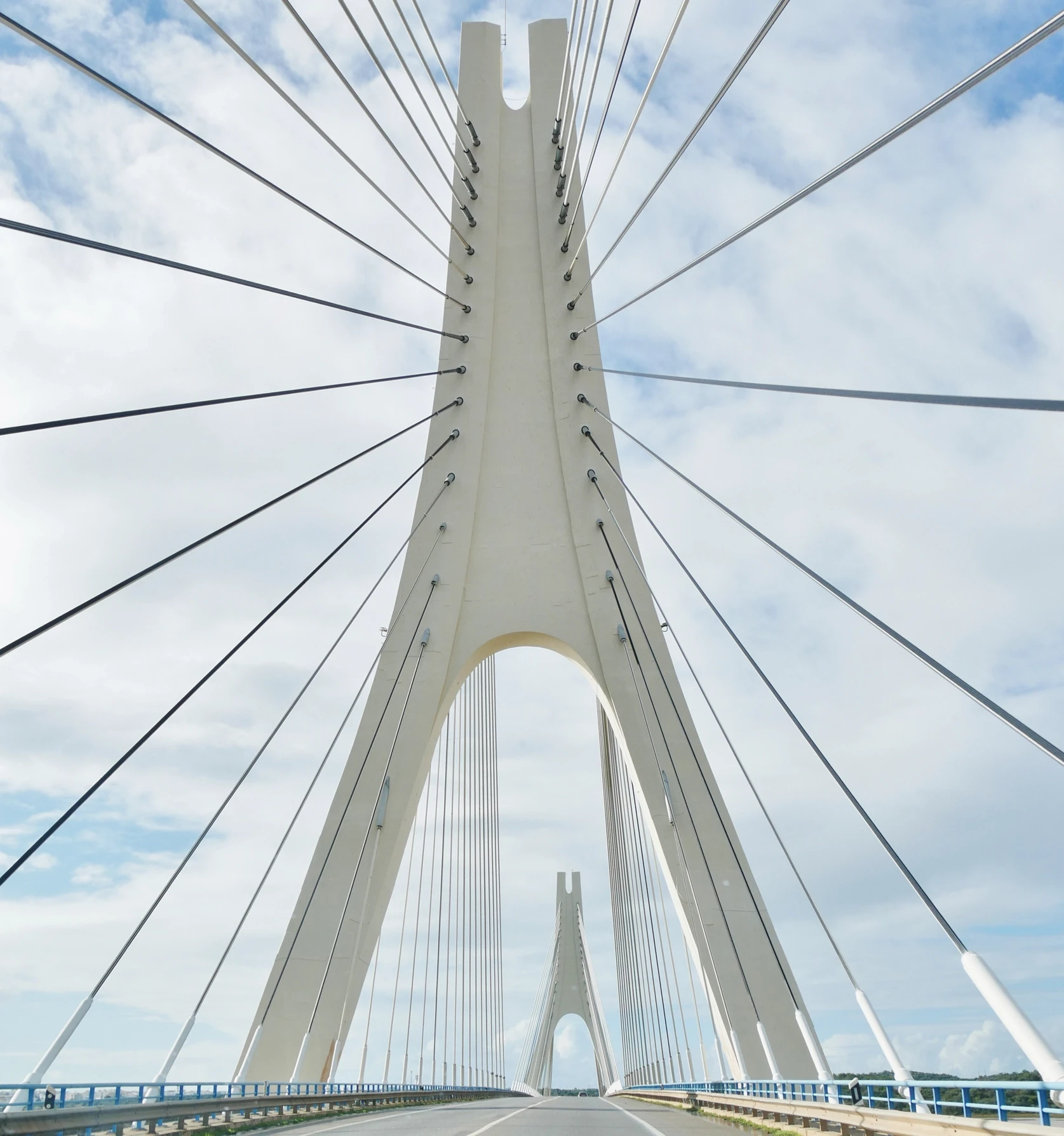 Cable-stayed bridge with a white tower against a cloudy sky.