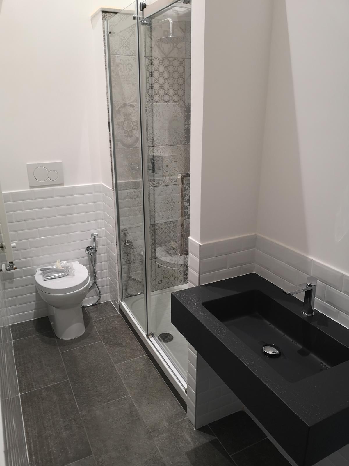 Bagno ristrutturato con piastrelle basse e box doccia in muratura e lavandino nero opaco moderno