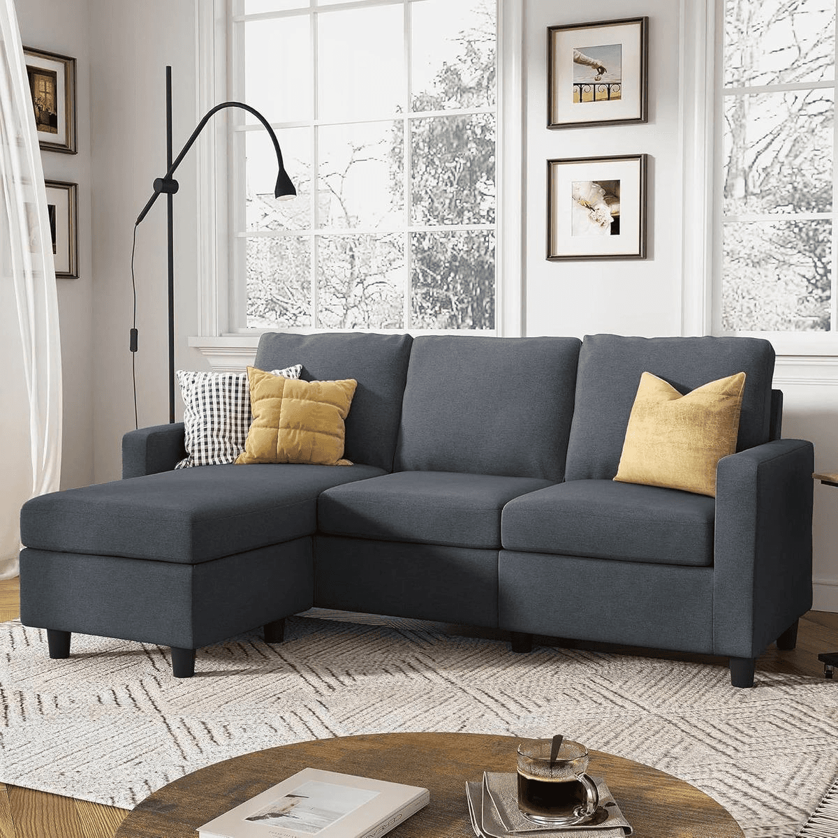 Dark gray Honbay convertible sectional sofa with yellow & patterned pillows in a cozy living room with large windows