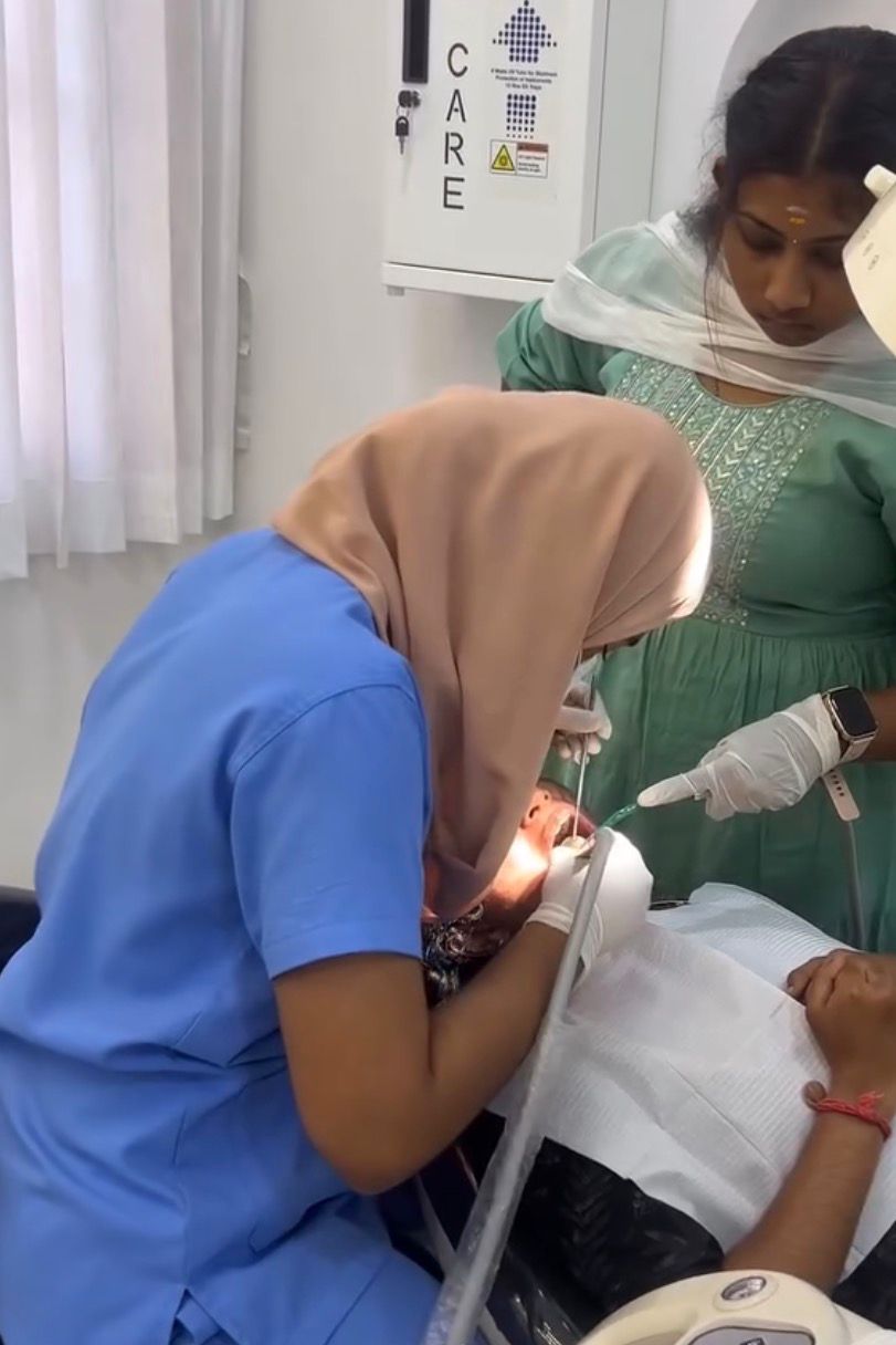 Healthcare professional in teal scrubs standing indoors with soft-focus background and hanging light