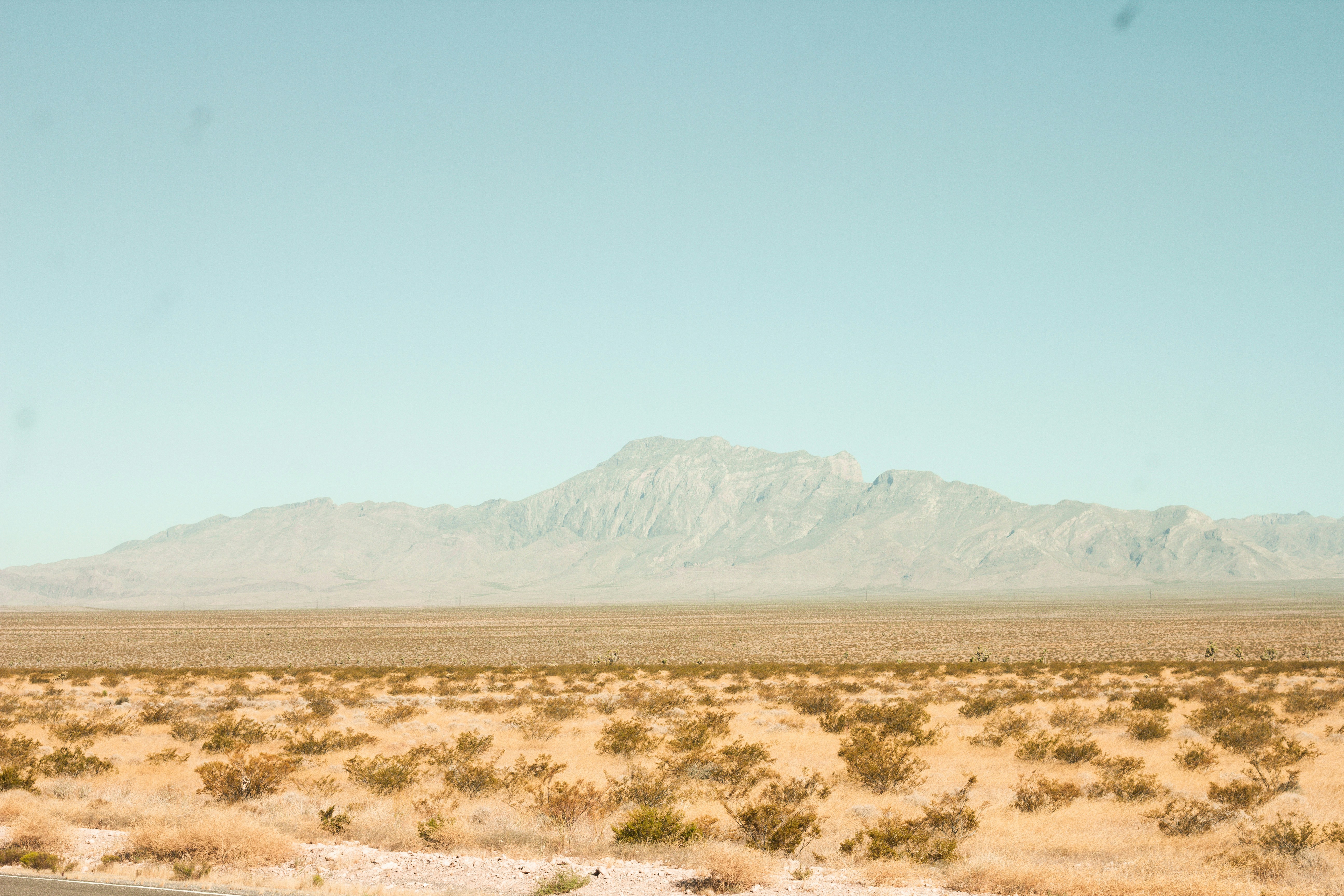 brown field near mountain under blue sky during daytime