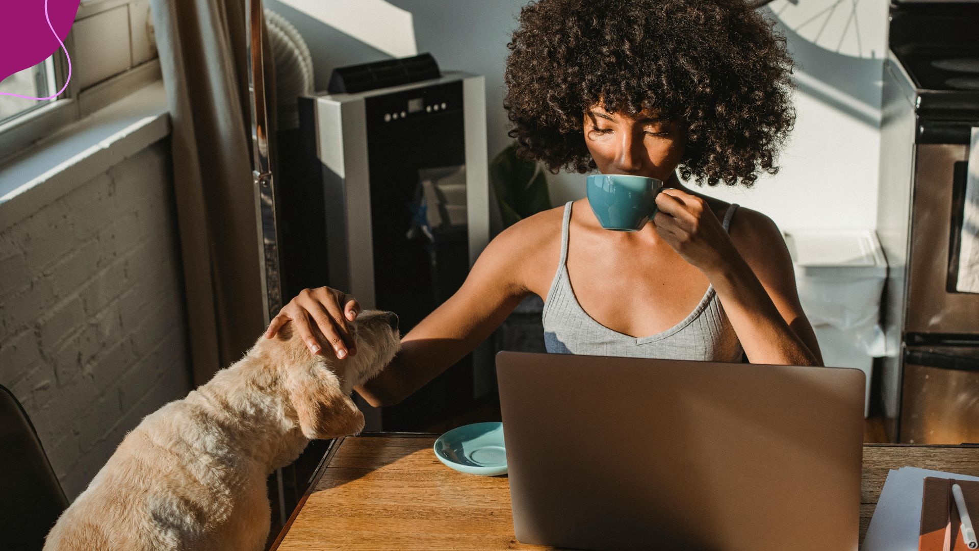 Woman sitting at a desck petting her doag and drinking coffee while reading her computer