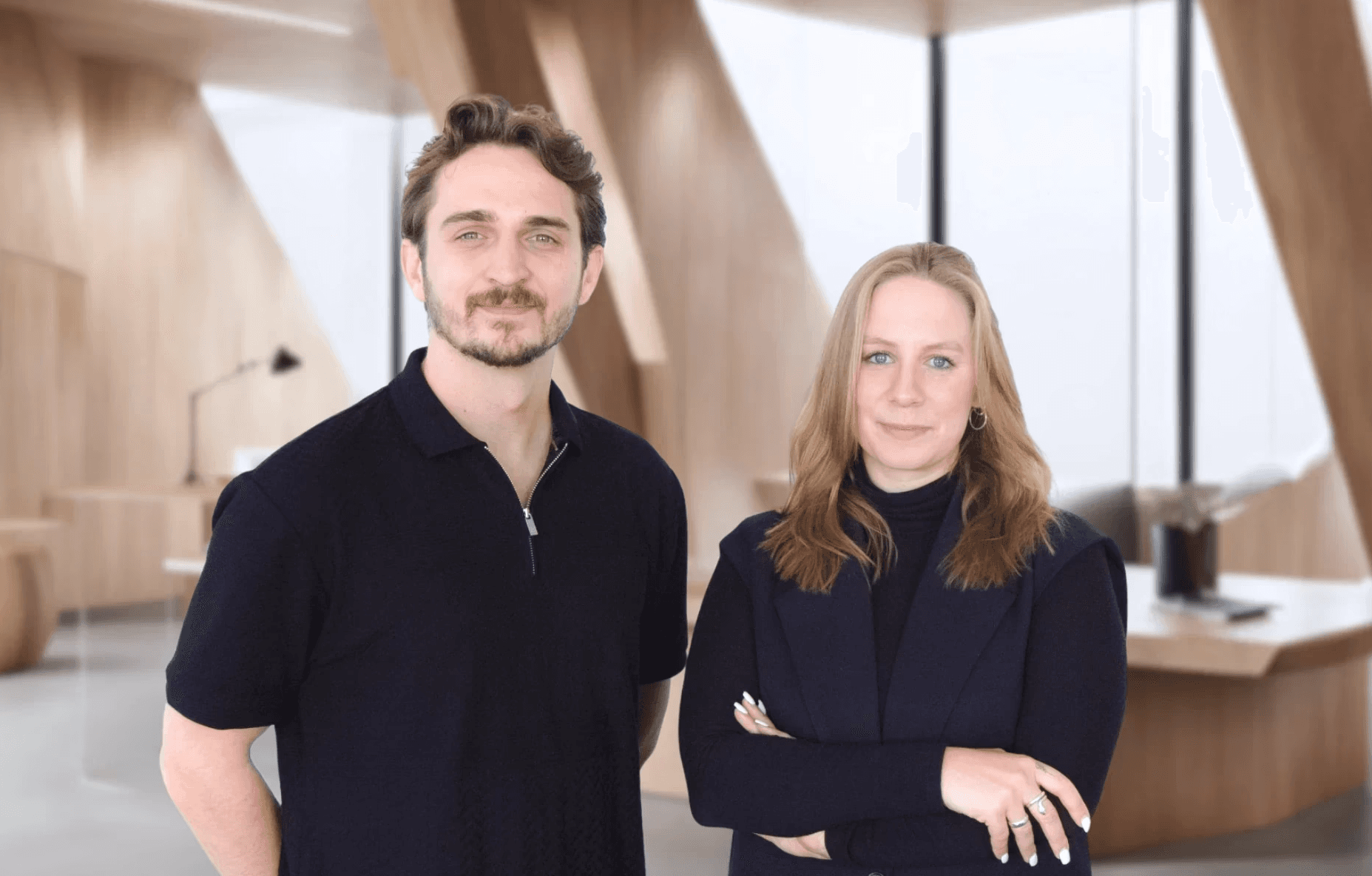 Jonas Behrend und Jamie Hartmann, Co-CEOs von Careship, Portrait eines Mannes und einer Frau stehend in einem modernen Büro mit Holzarchitektur.