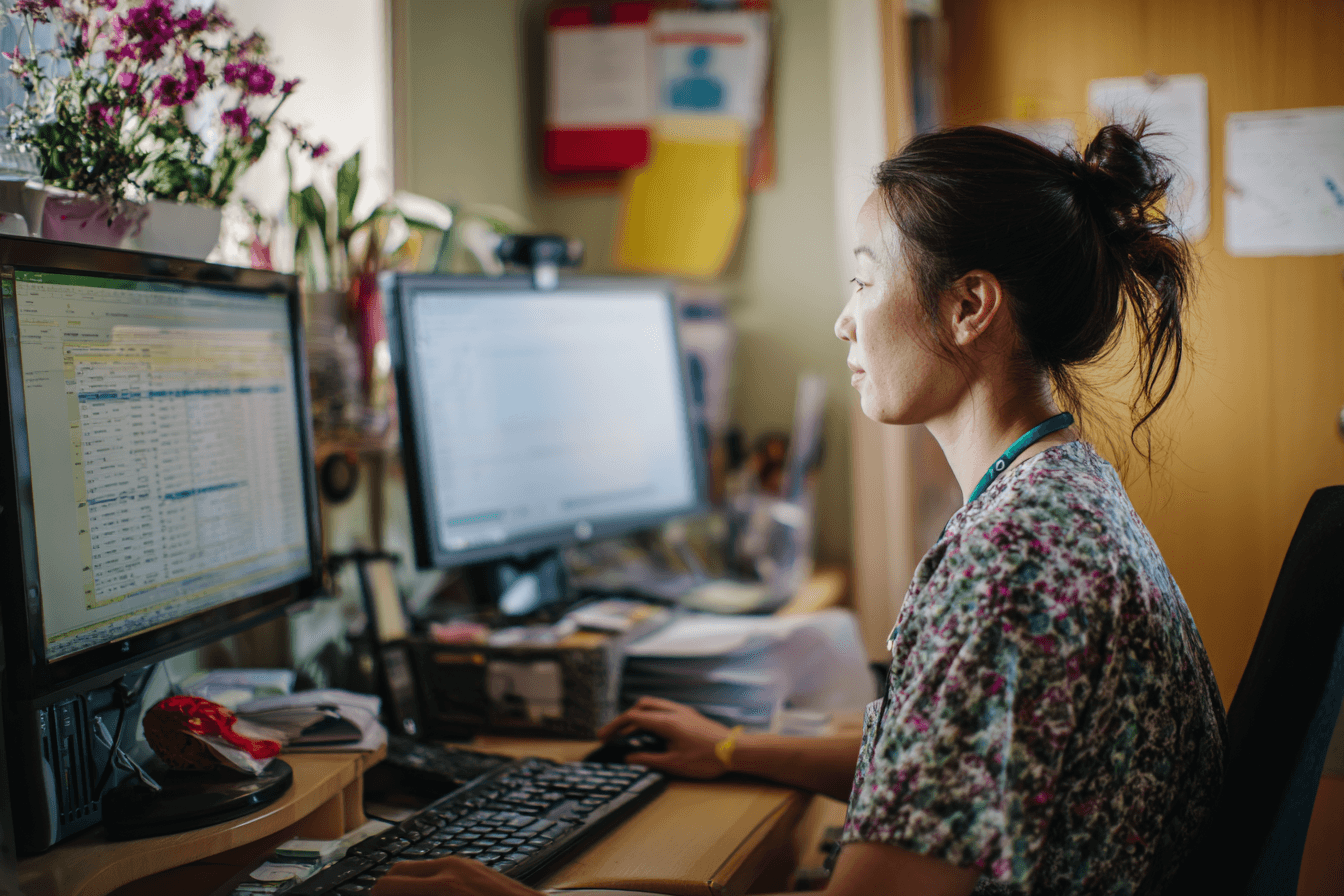 a woman in her 30s, doing manual data entry on a desktop in a home care agency office.