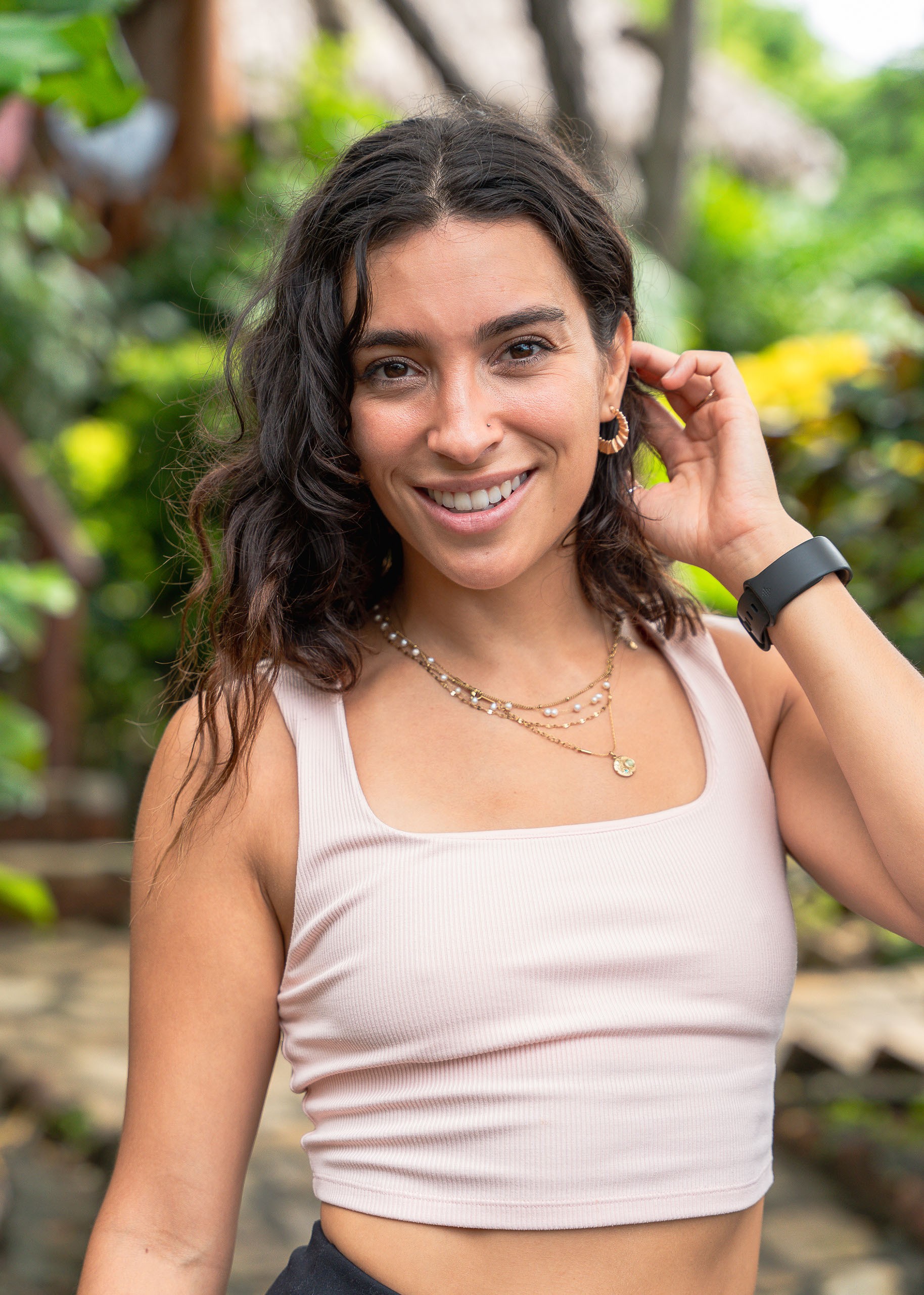 Confident man standing in a greenhouse surrounded by lush green plants, wearing a beige shirt and neutral-toned outfit.