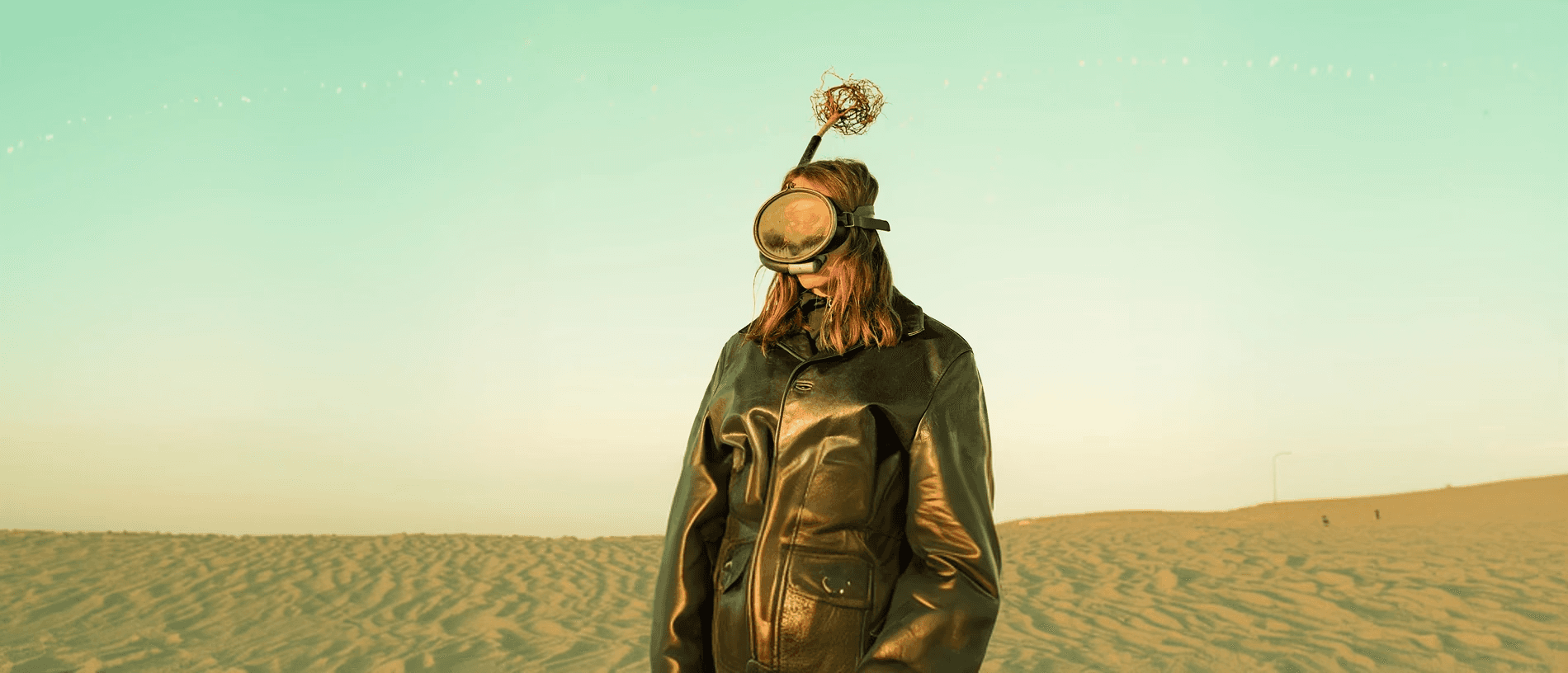 A person wearing a mask with an antenna standing against a pale sky.