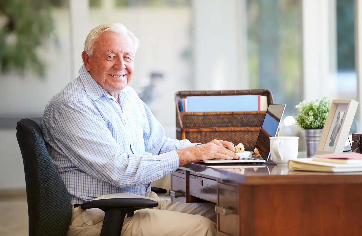 An older man sits at his desk with his laptop.