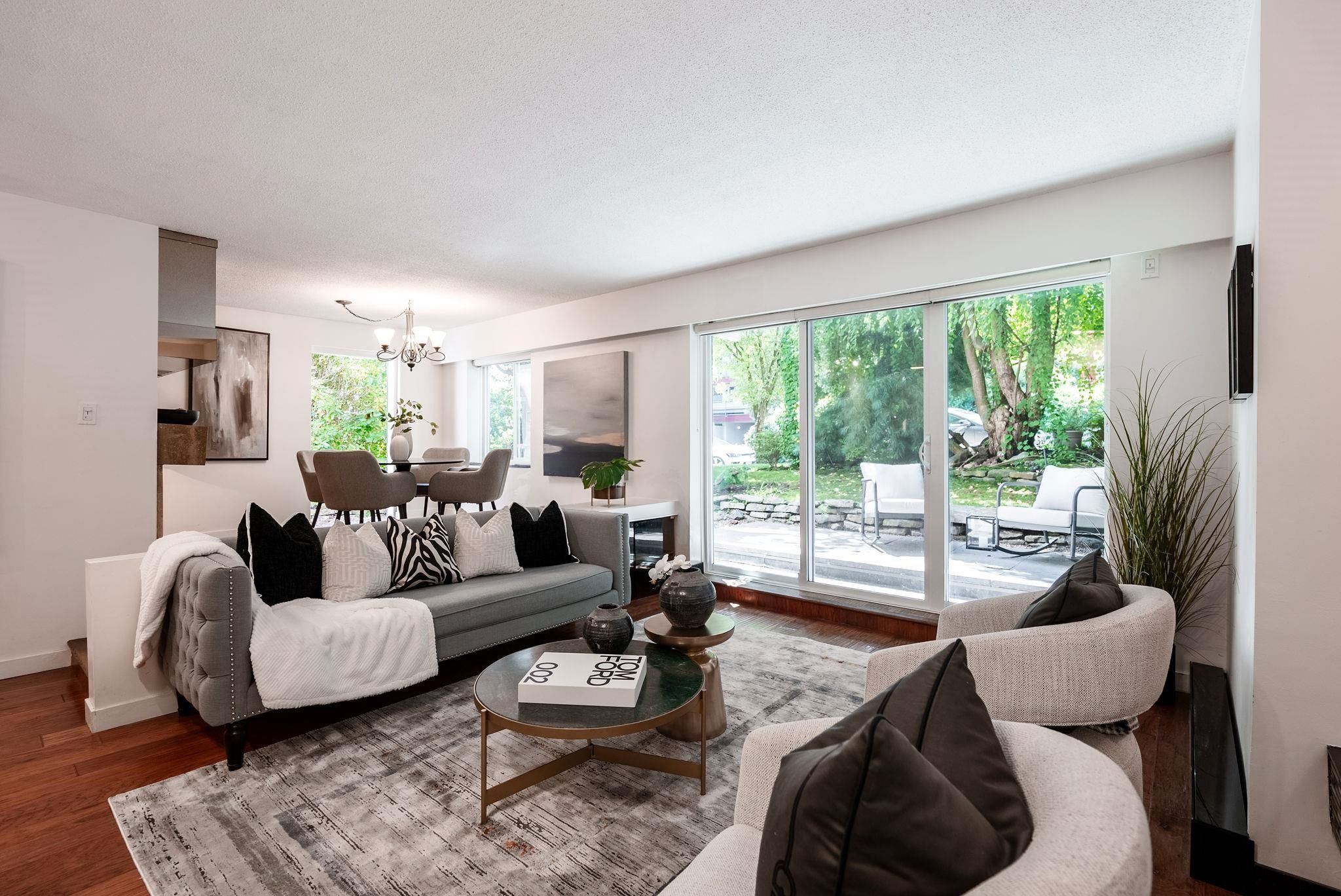 Modern living room with a light color scheme, comfortable seating, and large windows showing greenery outside.