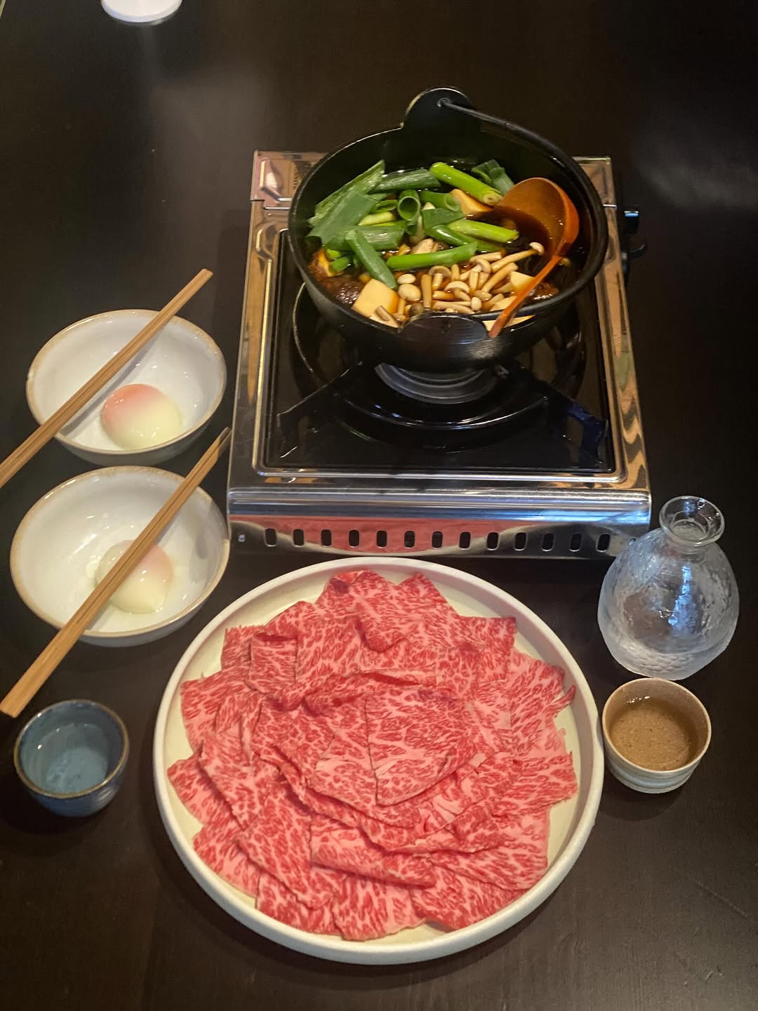 Person with a mustache wearing a black t-shirt carrying a tall stack of pizza boxes inside a dimly lit bar or restaurant.