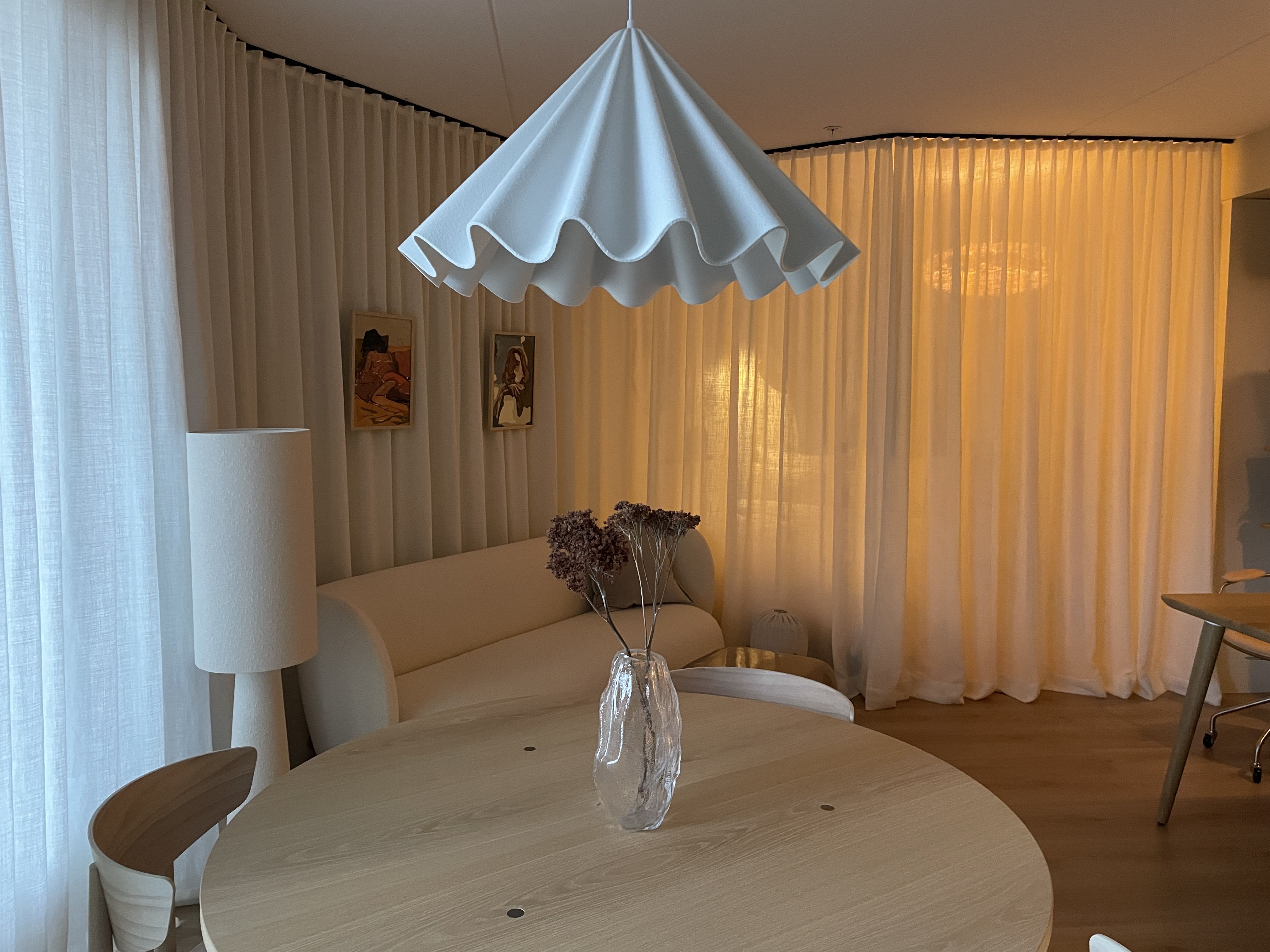 Round dining table beneath a white sculptural pendant, with a cream sofa and curtains behind it.