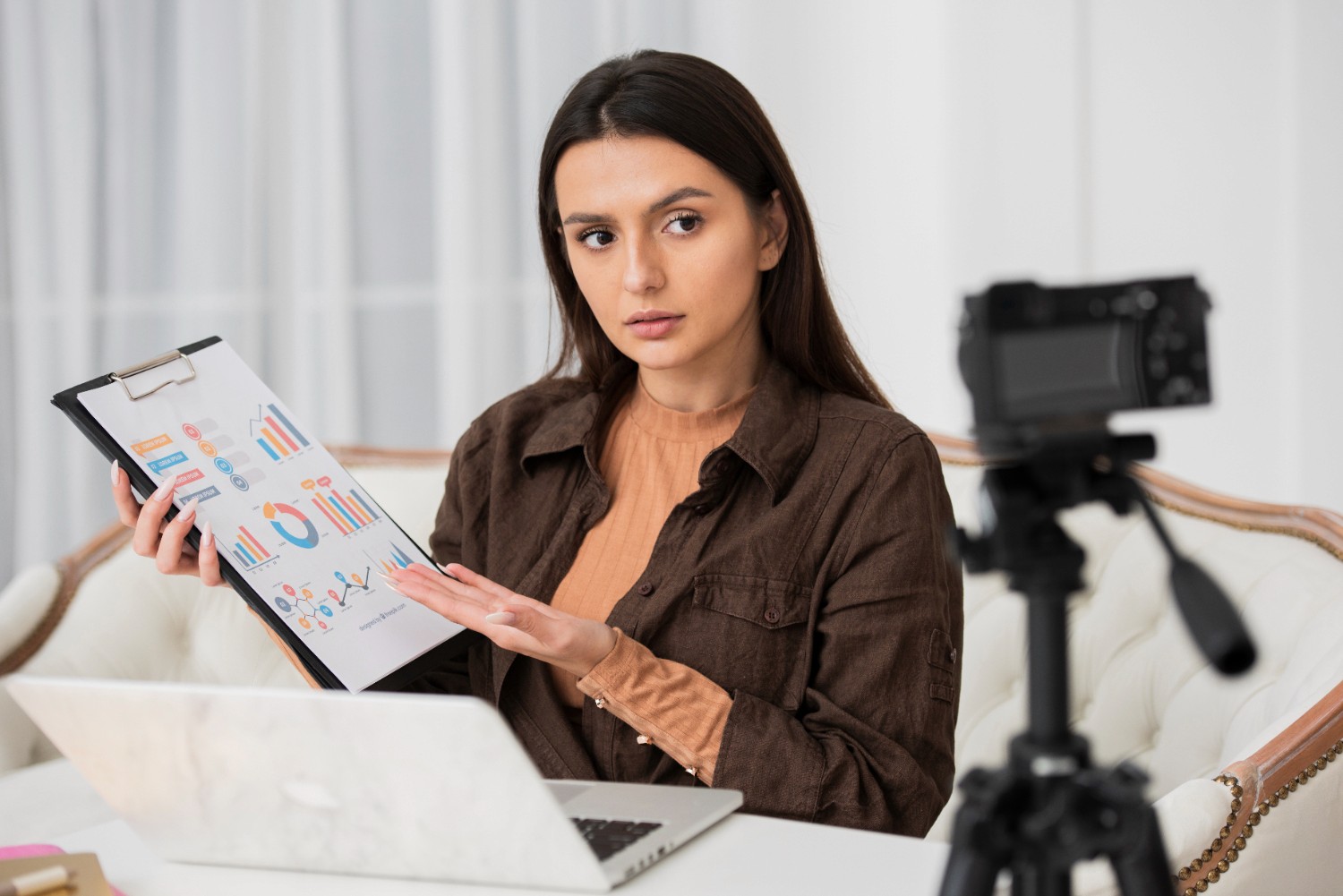 A woman with a clipboard examines a laptop, showcasing a blend of organization and technology in her workspace.