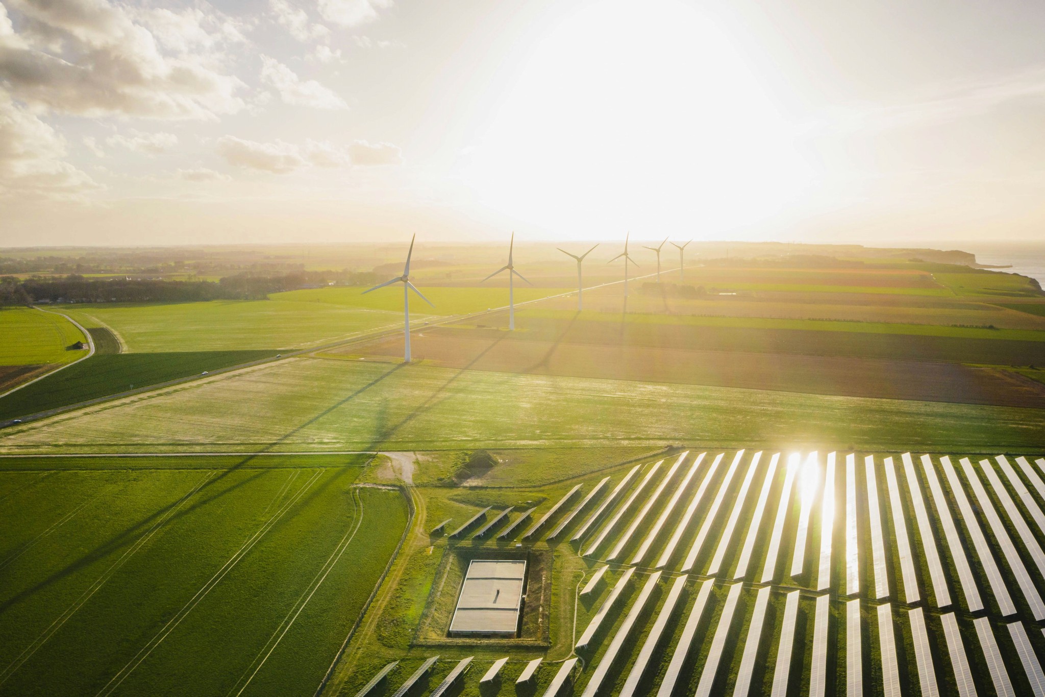 Ein malerischer Blick auf eine nachhaltige Energielandschaft mit Windturbinen und Solarpanelen unter einem hellen, sonnendurchfluteten Himmel, der die Integration erneuerbarer Energietechnologien zeigt.