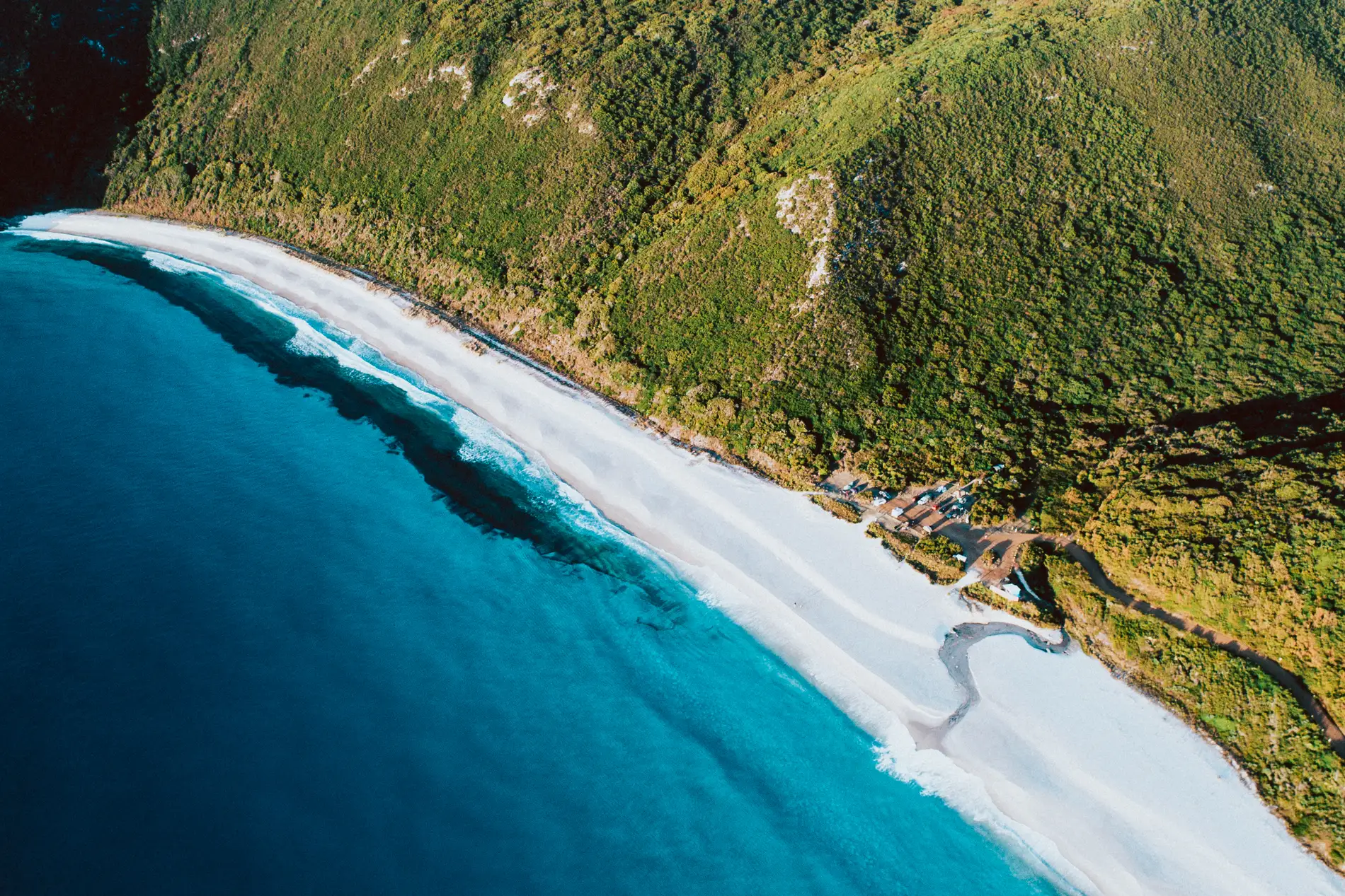 Aerial of a long white beach curving beneath steep green hills