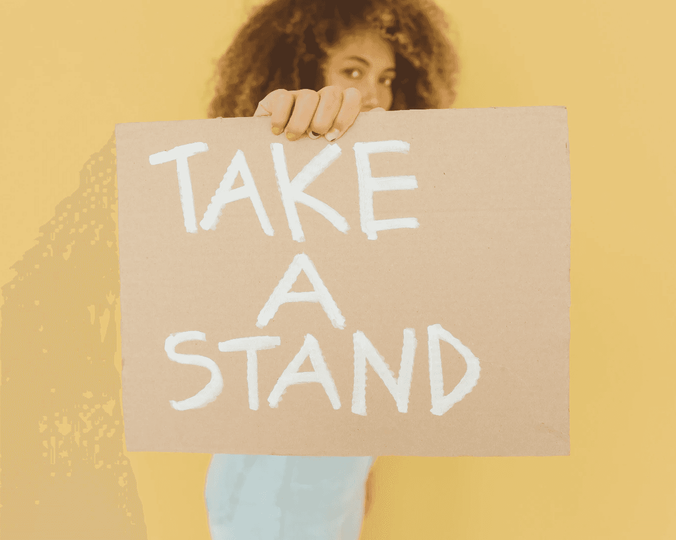 A person holds up a sign that reads "TAKE A STAND" against a yellow background.