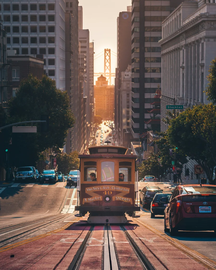 San Francisco cable car climbing a city street with the Bay Bridge in the distance.