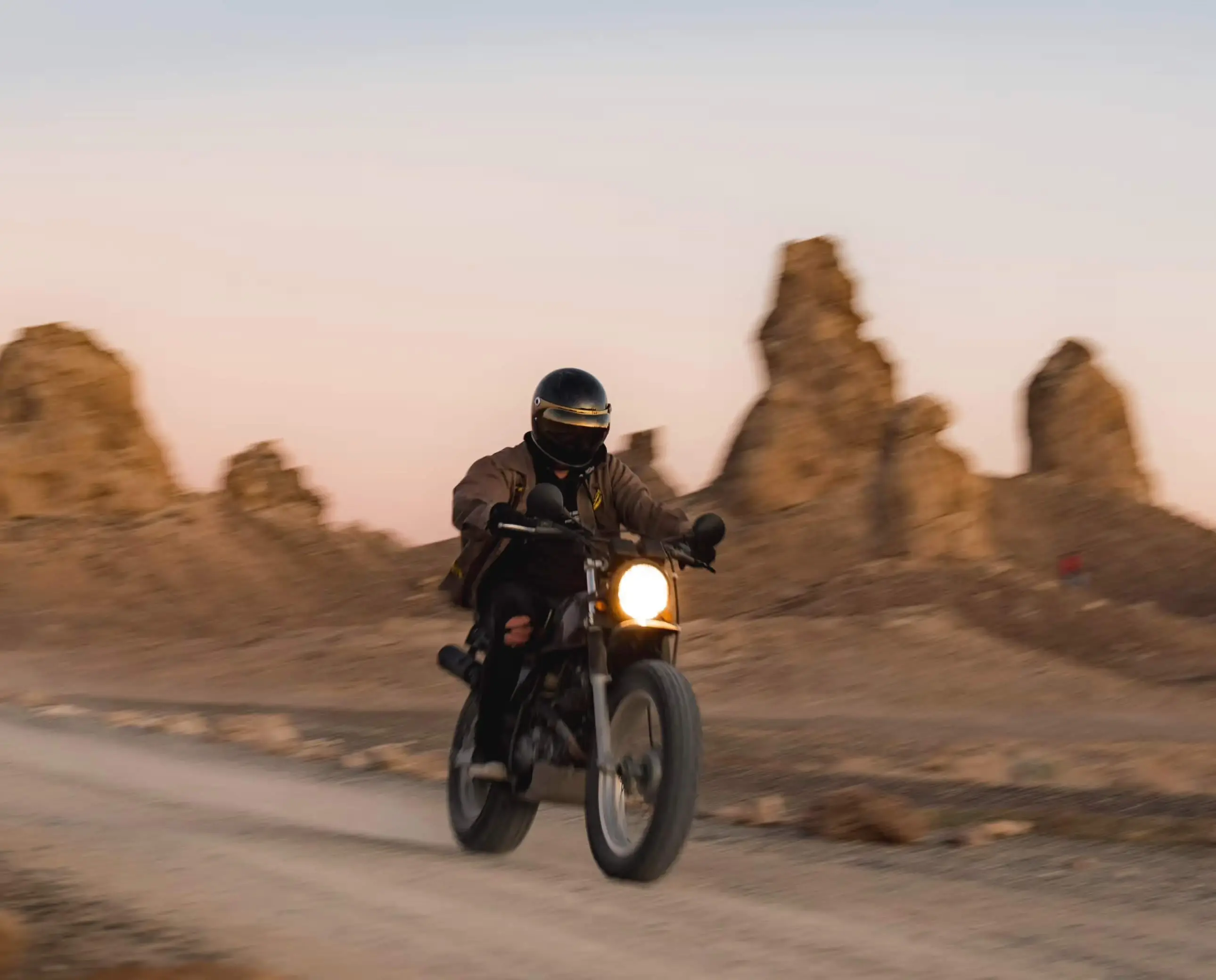Motard roulant dans un paysage désertique au coucher du soleil, illustrant la liberté et l’aventure à moto.