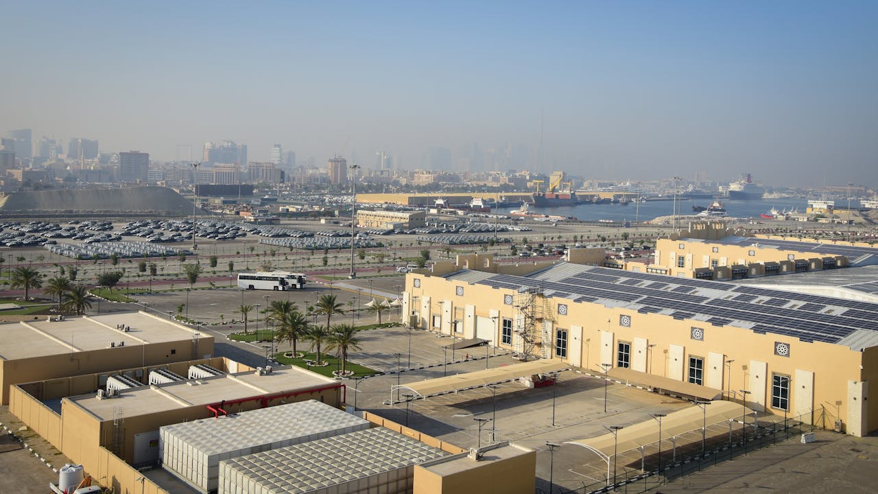 Aerial view of the Jebel Ali port  with warehouses, solar panels, port facilities, and Dubai skyline in the background.